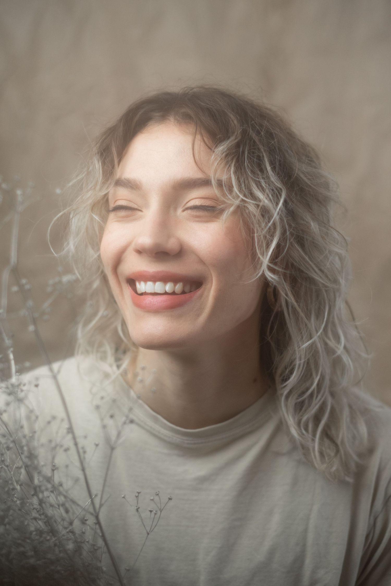 Artistic portrait with soft lighting showing wavy blonde hair and a genuine smile.