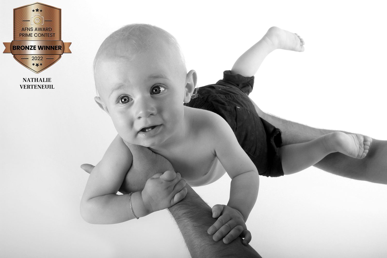 A black and white studio portrait of a baby lying on their stomach.