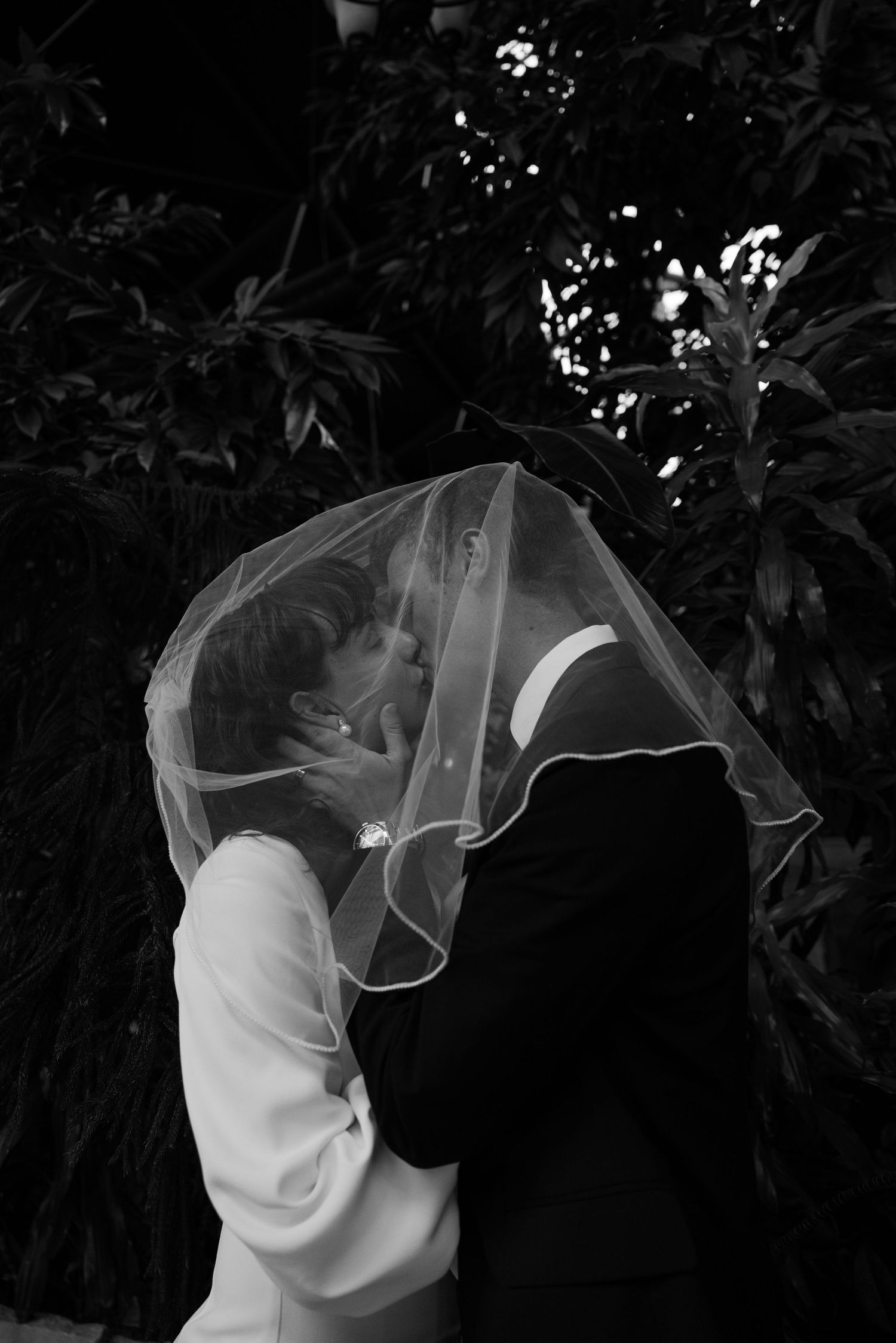 Romantic couple sharing an intimate moment under a delicate veil in black and white.