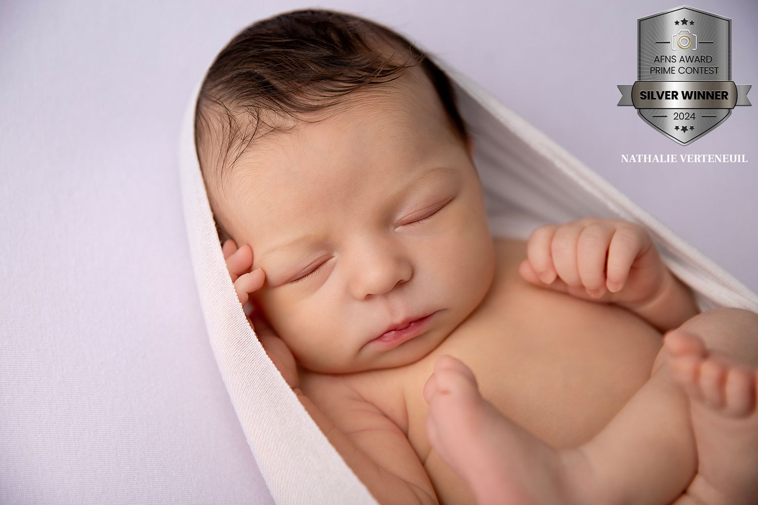 A sleeping newborn baby wrapped in soft pink fabric against a purple background.