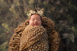 A newborn sleeps peacefully in a brown knitted wrap with white polka dots against a dark background.
