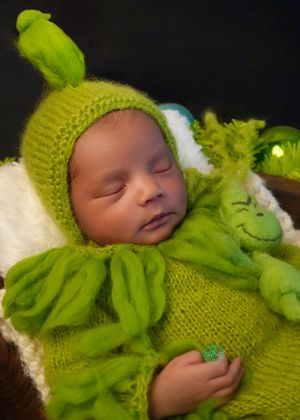 A sleeping baby wearing a bright lime green knitted hat and outfit against a white background.