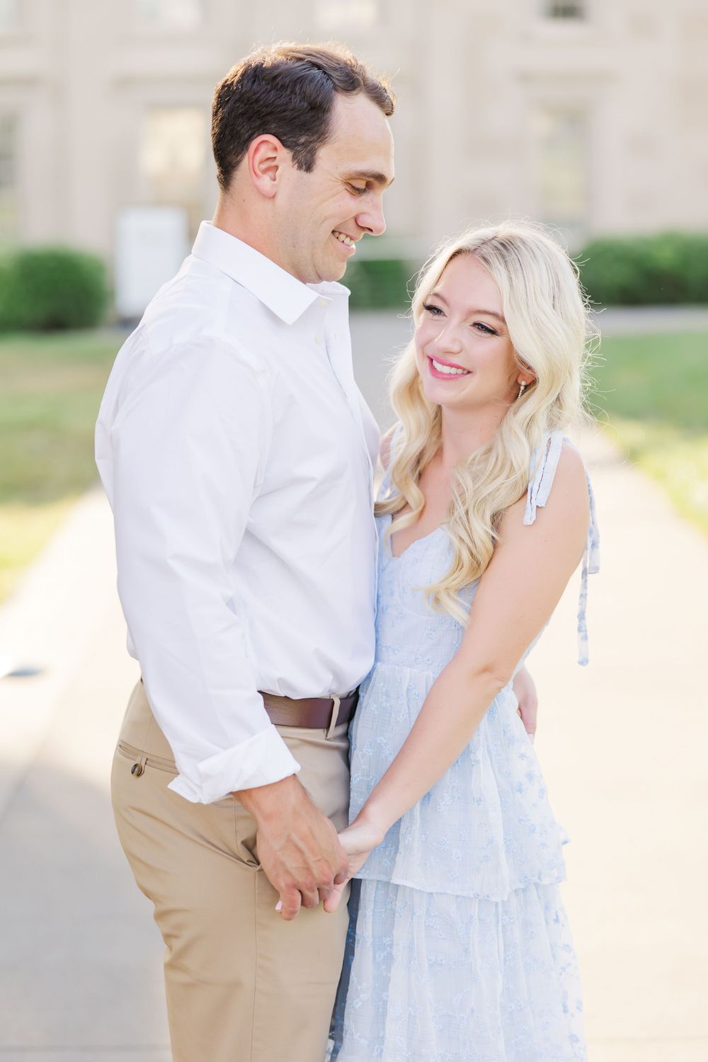 A romantic couple poses outdoors wearing coordinated white and light blue outfits for an engagement photoshoot.