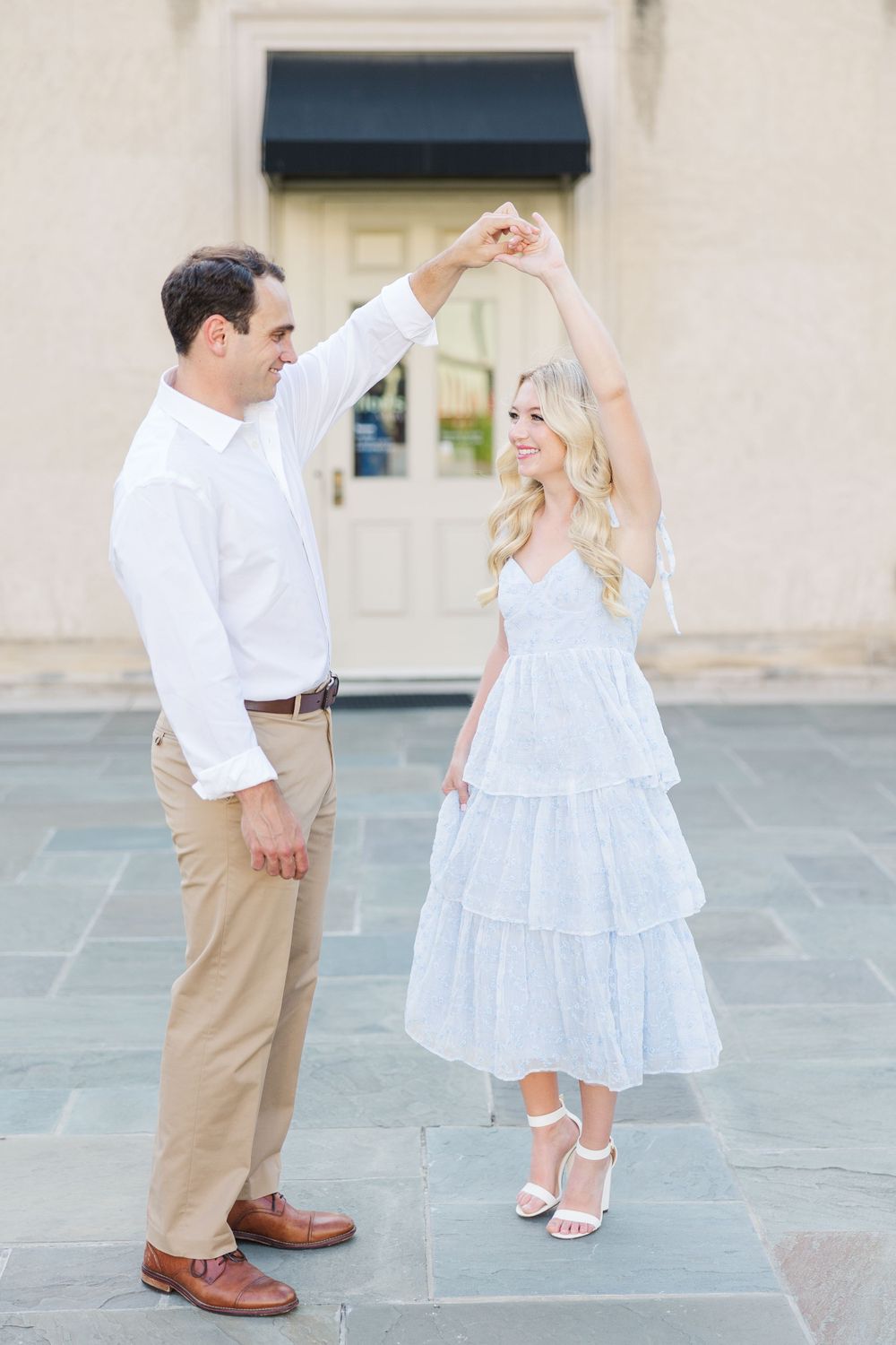 A couple dances on stone pavement with the man twirling his partner in a light blue tiered dress.