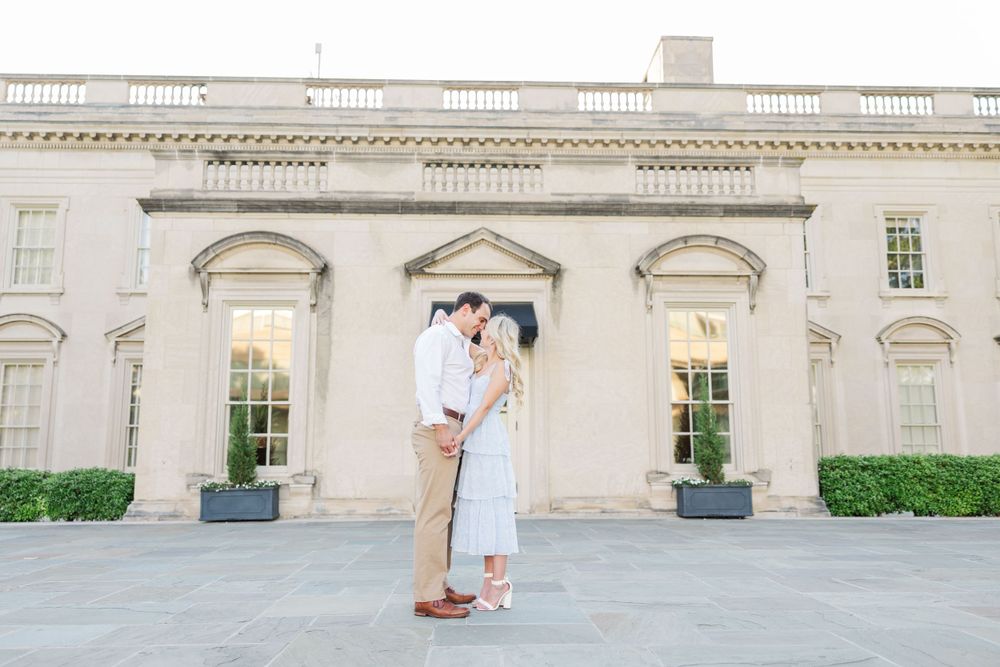 A couple poses in front of a grand historic building for their engagement photos.