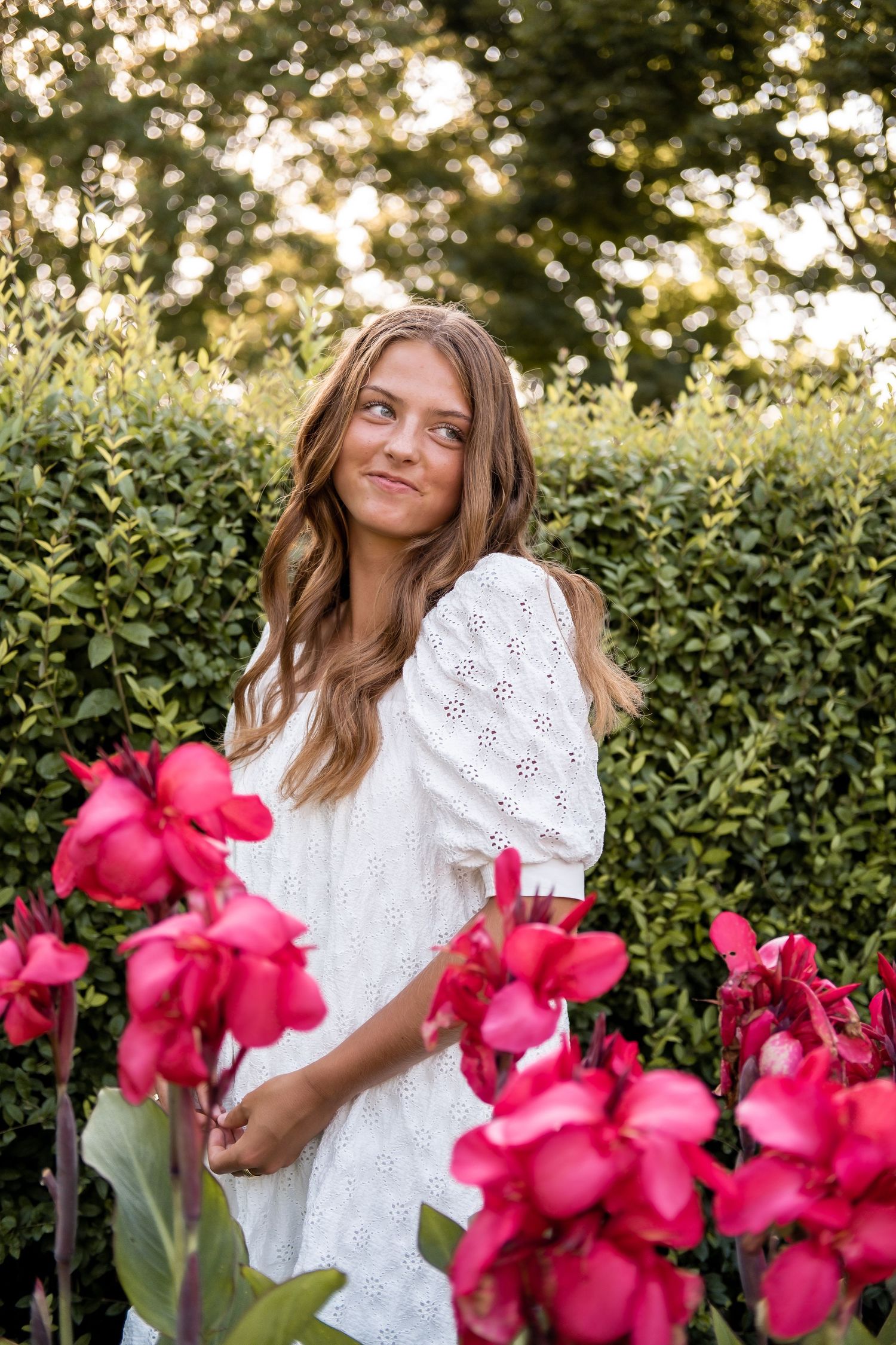 White eyelet dress contrasts beautifully with vibrant pink flowers in a garden setting.