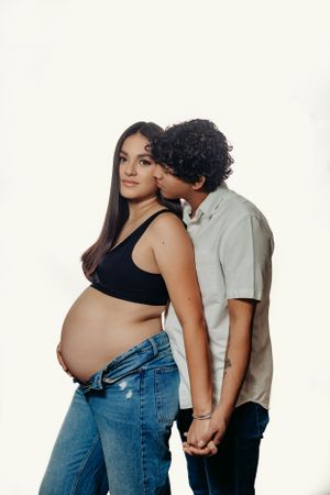 Intimate maternity photo of expecting couple holding hands against white background.