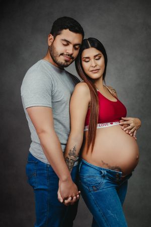 Expecting couple in casual attire share tender moment during maternity photoshoot.