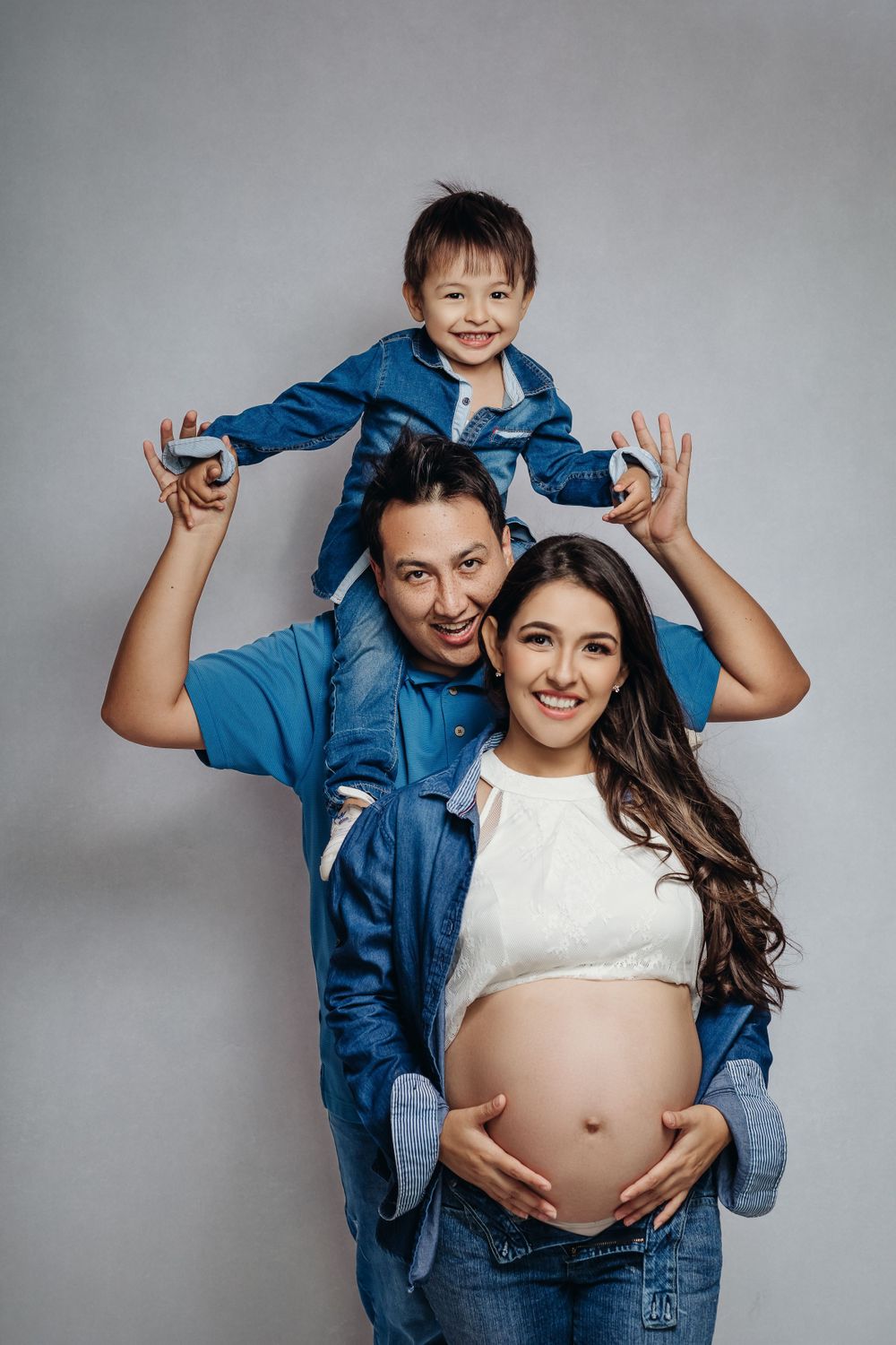 Joyful family studio portrait in coordinating denim outfits against grey background.