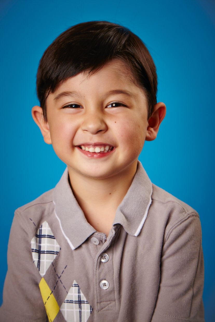 Portrait of young child in grey polo shirt with plaid detail against blue background.