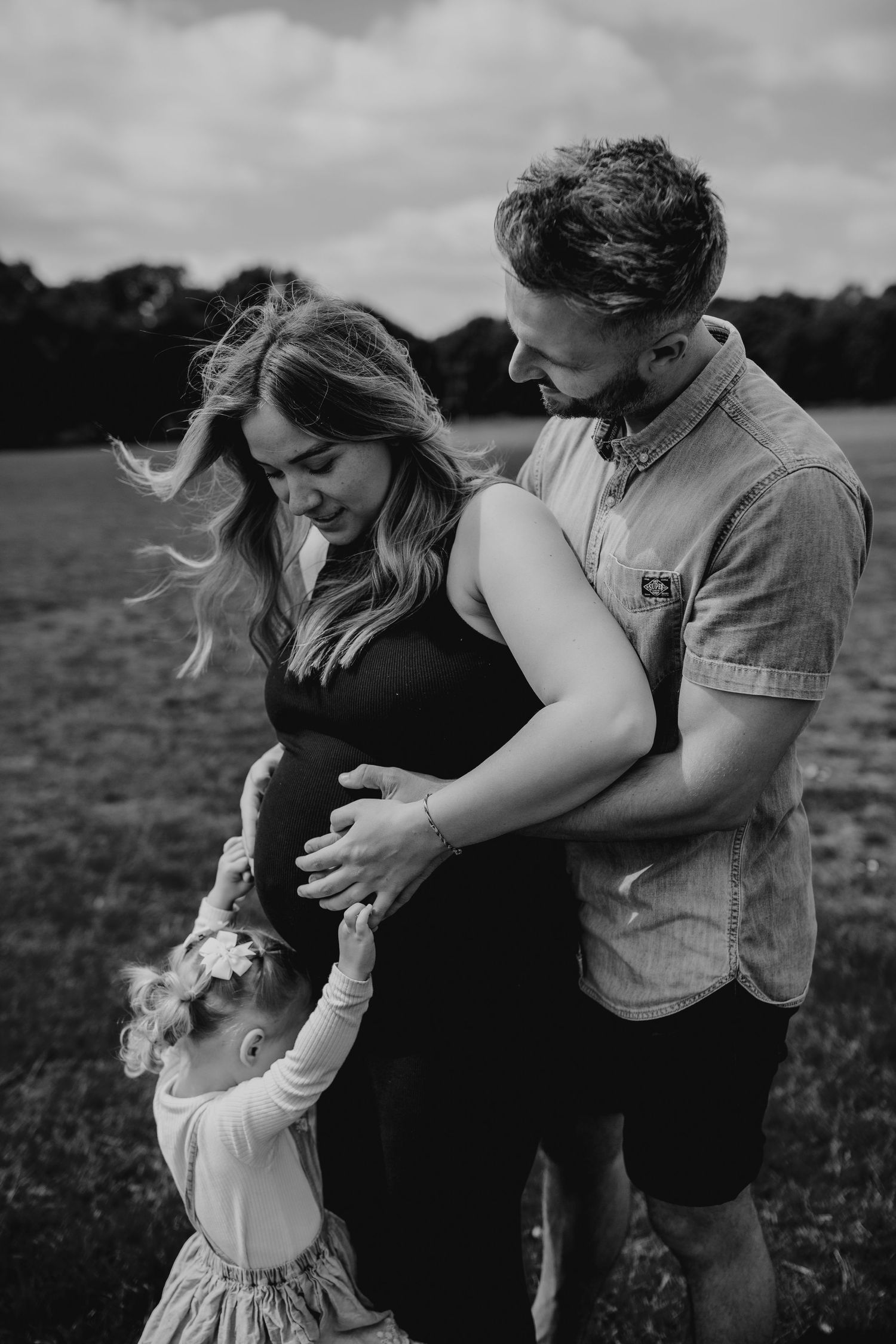 Family sharing tender moment together in field during black and white photoshoot. Essex family photographer