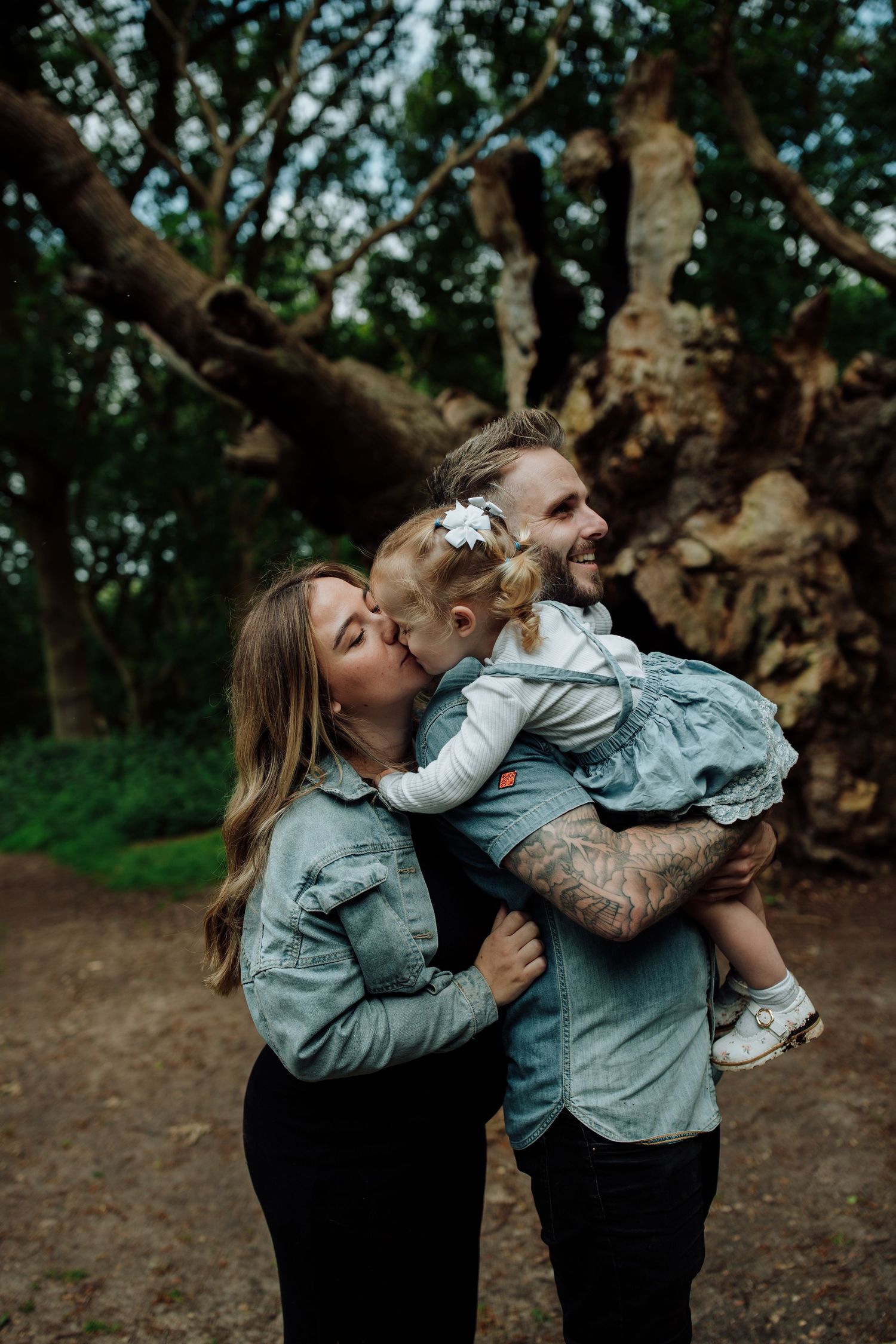 Family sharing intimate moment together against large tree in forest setting. Essex family photographer