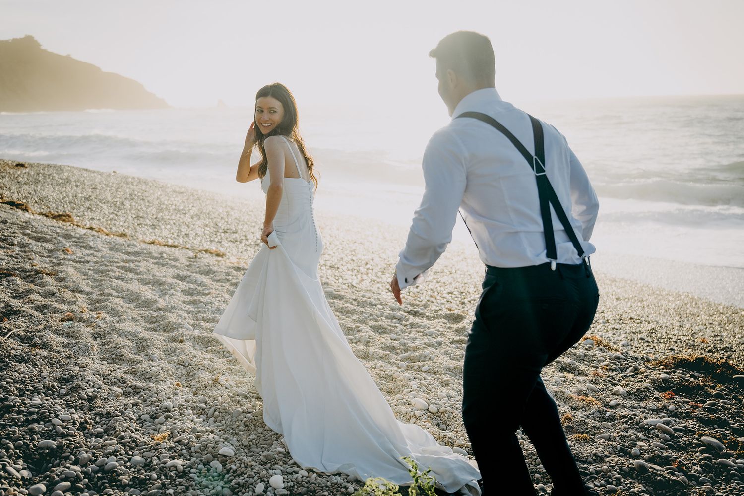 Pareja de recién casados caminando por una playa de Asturias al atardecer durante una sesión de postboda fotografiada por Juan Llavio