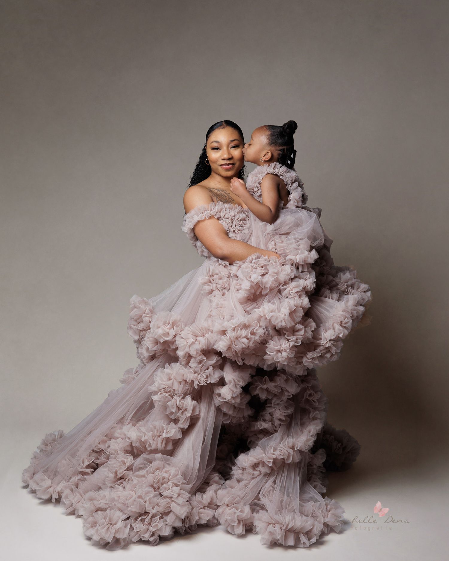 Elegant studio portrait of mother and child wearing matching voluminous pink gowns.