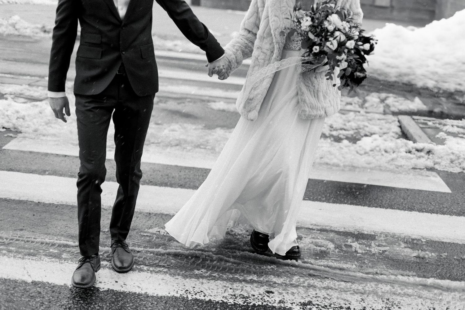 Wedding couple walking across a rainy crosswalk, with dress and veil flowing behind.
