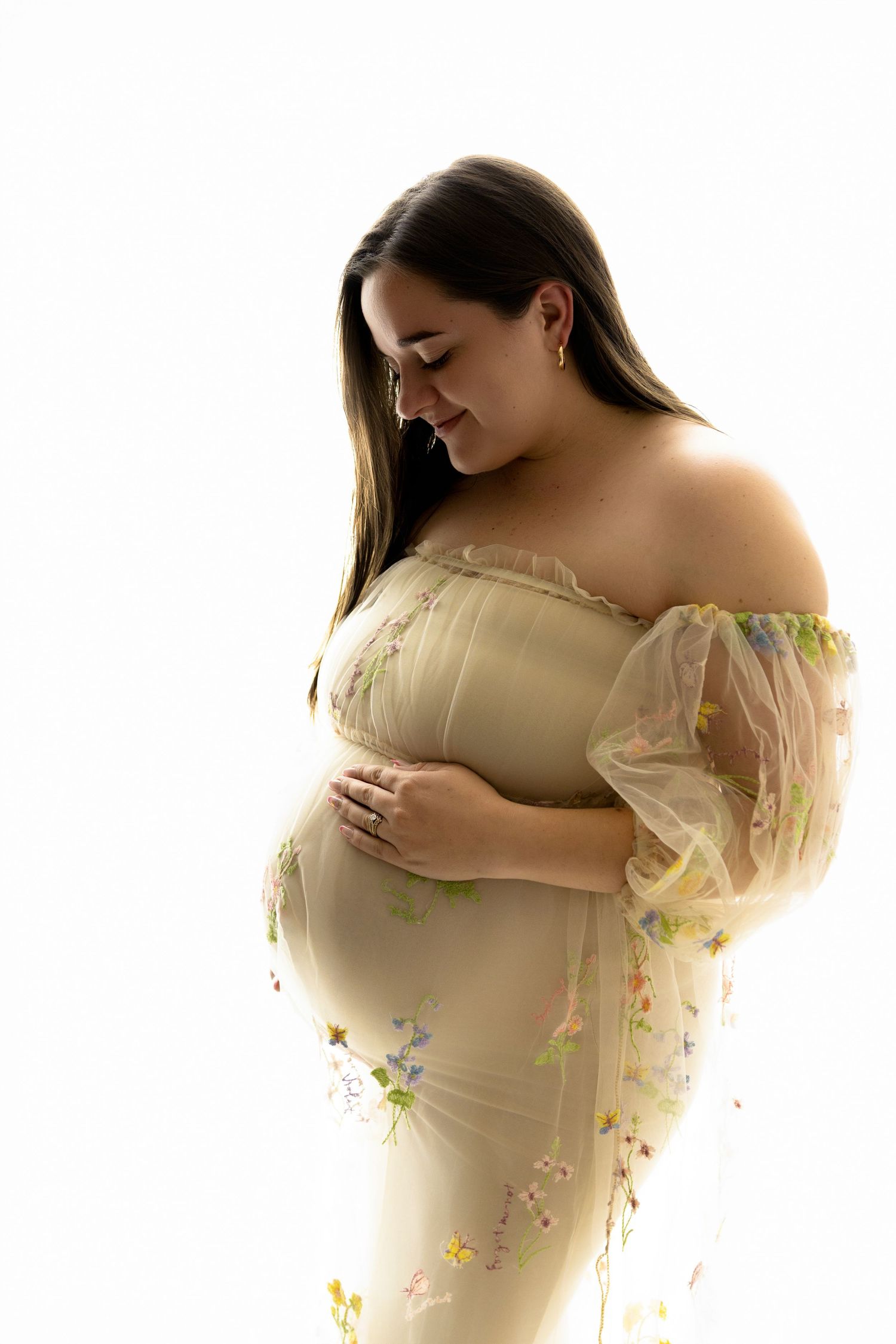 A woman with brown hair looking down at her baby bump with a happy face