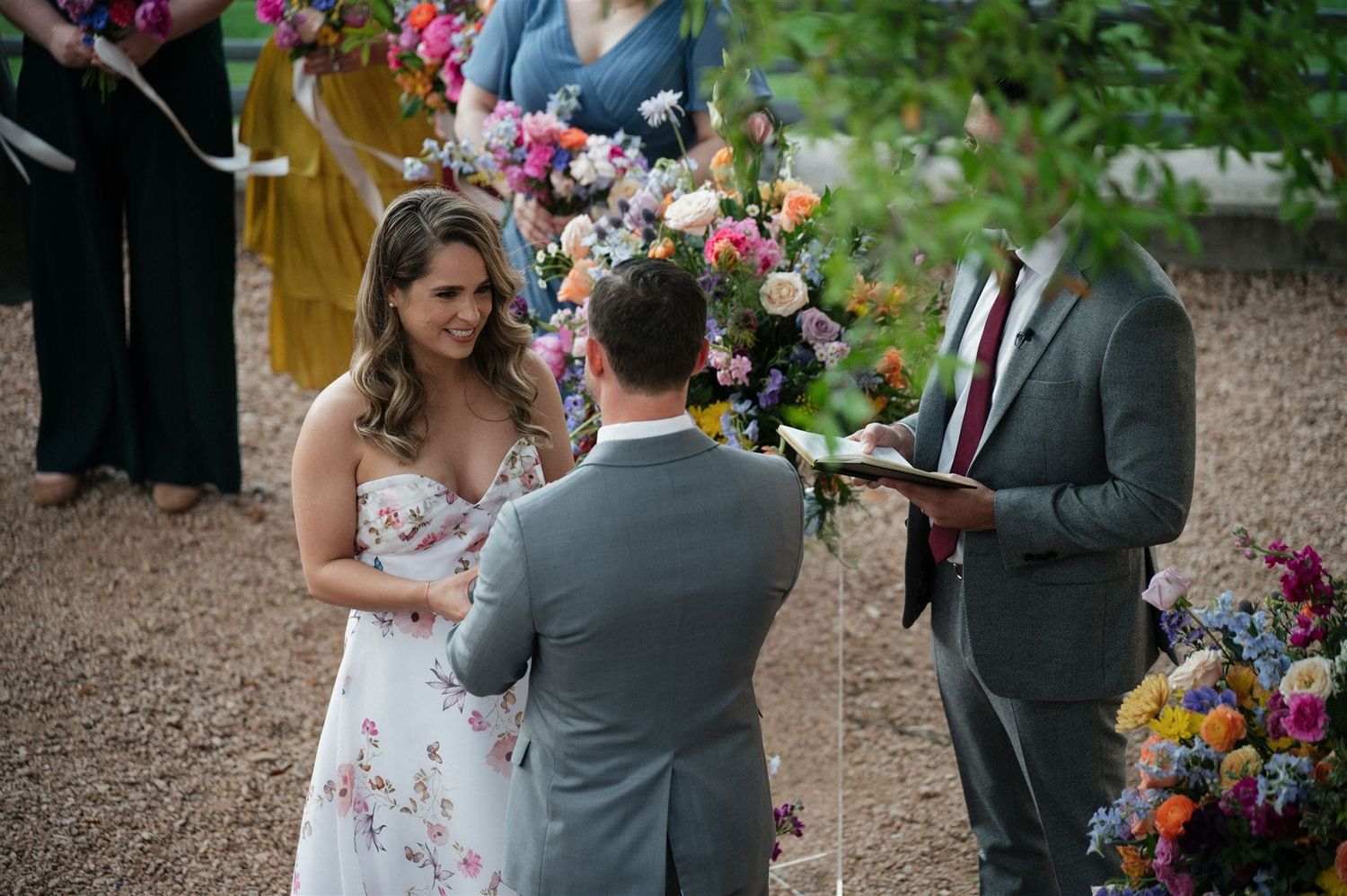 A romantic outdoor wedding ceremony takes place on a garden path surrounded by vibrant floral arrangements.