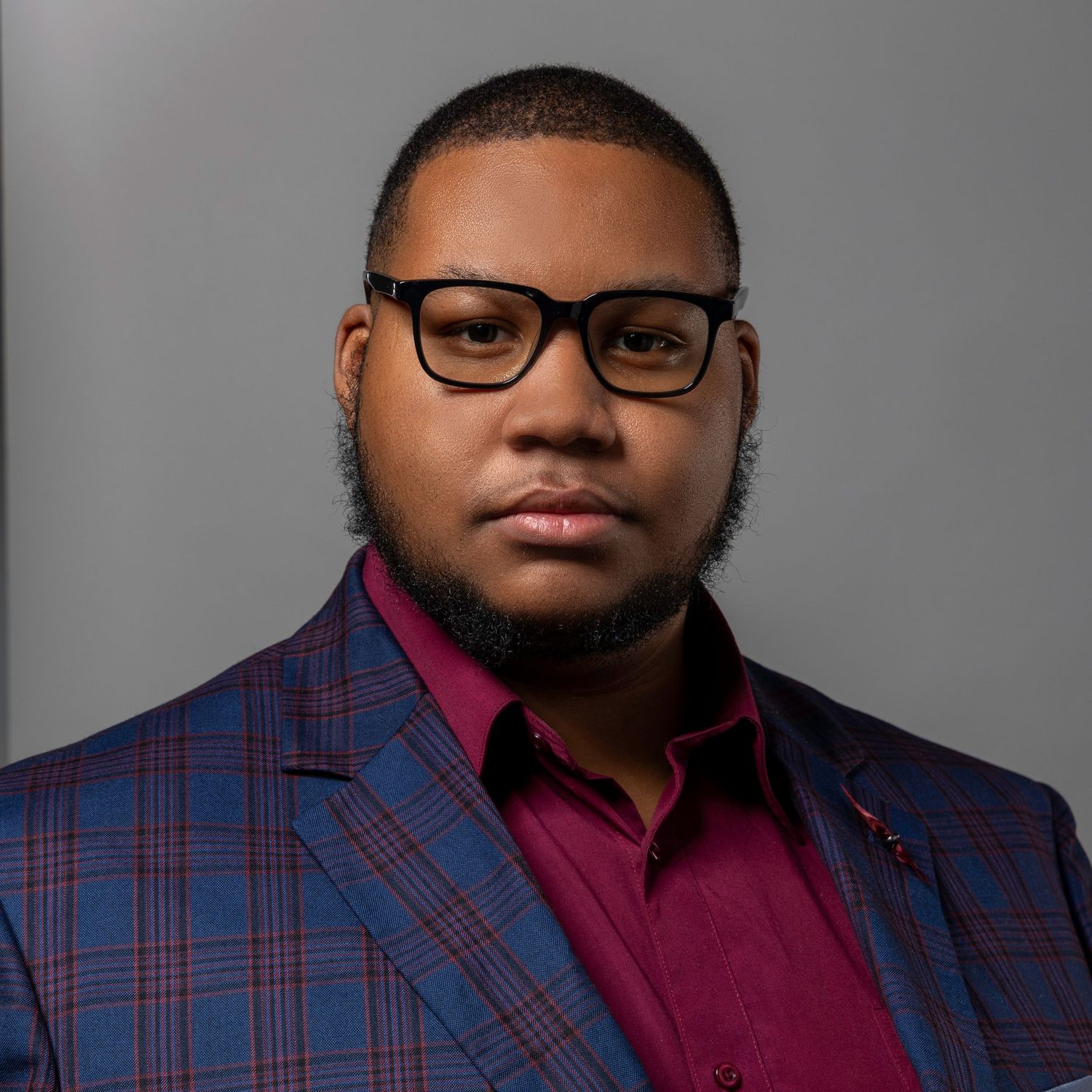 Professional man wearing glasses and blue plaid blazer poses for formal portrait headshot.