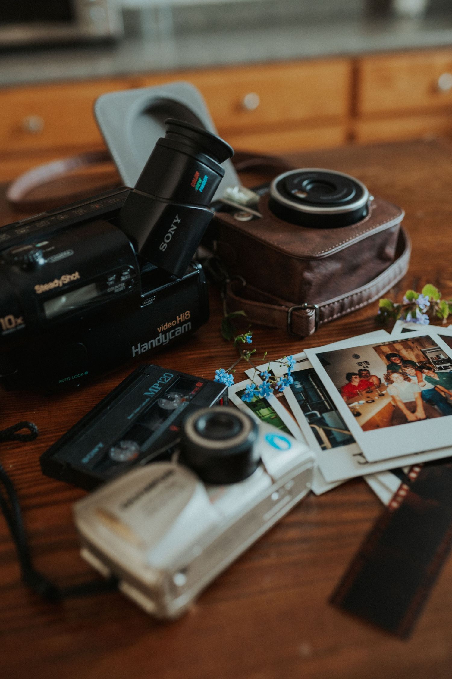 Vintage cameras and instant photos scattered on wooden surface with nostalgic film processing equipment.