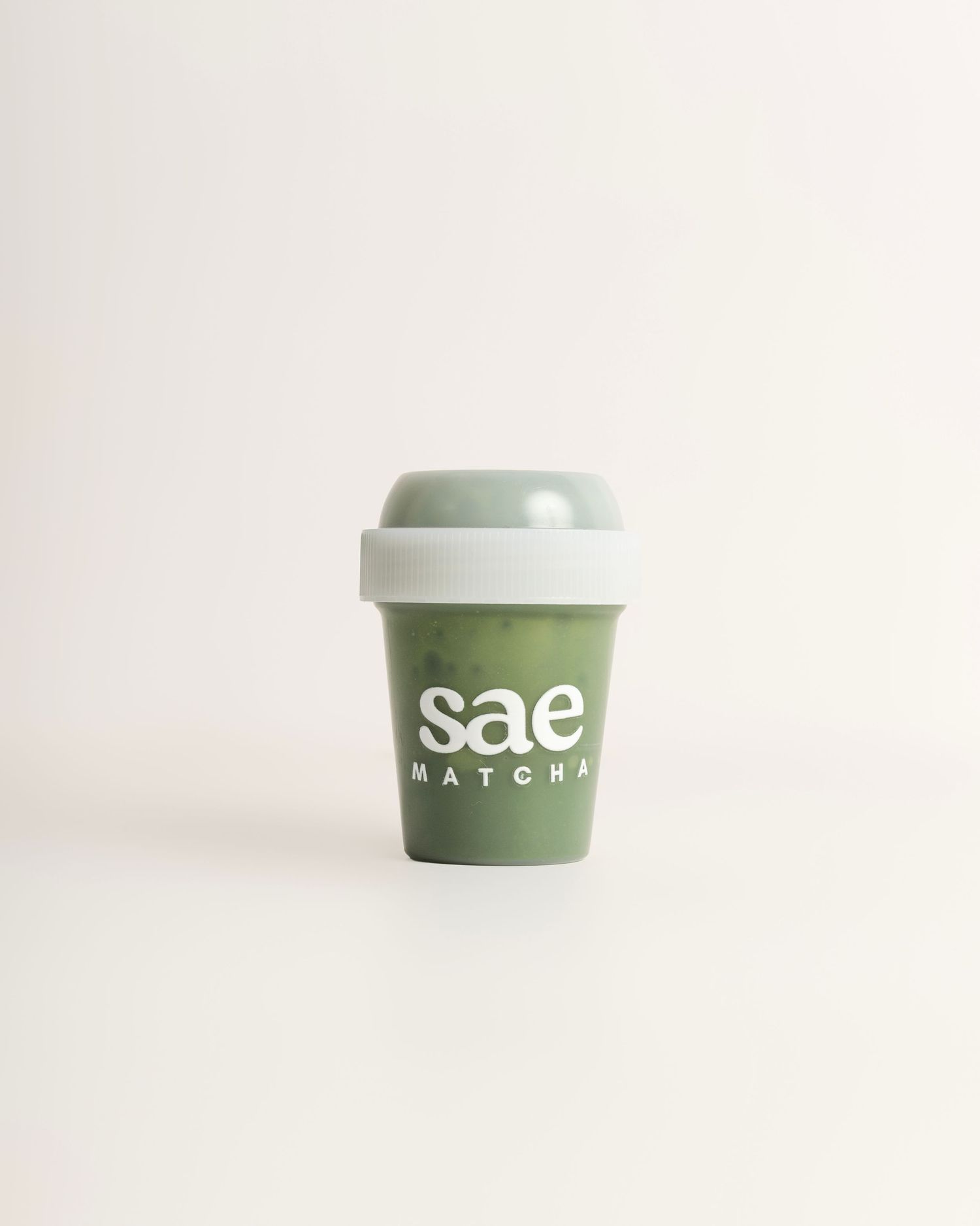 Sae Matcha branded reusable green coffee cup with light gray lid on white background.