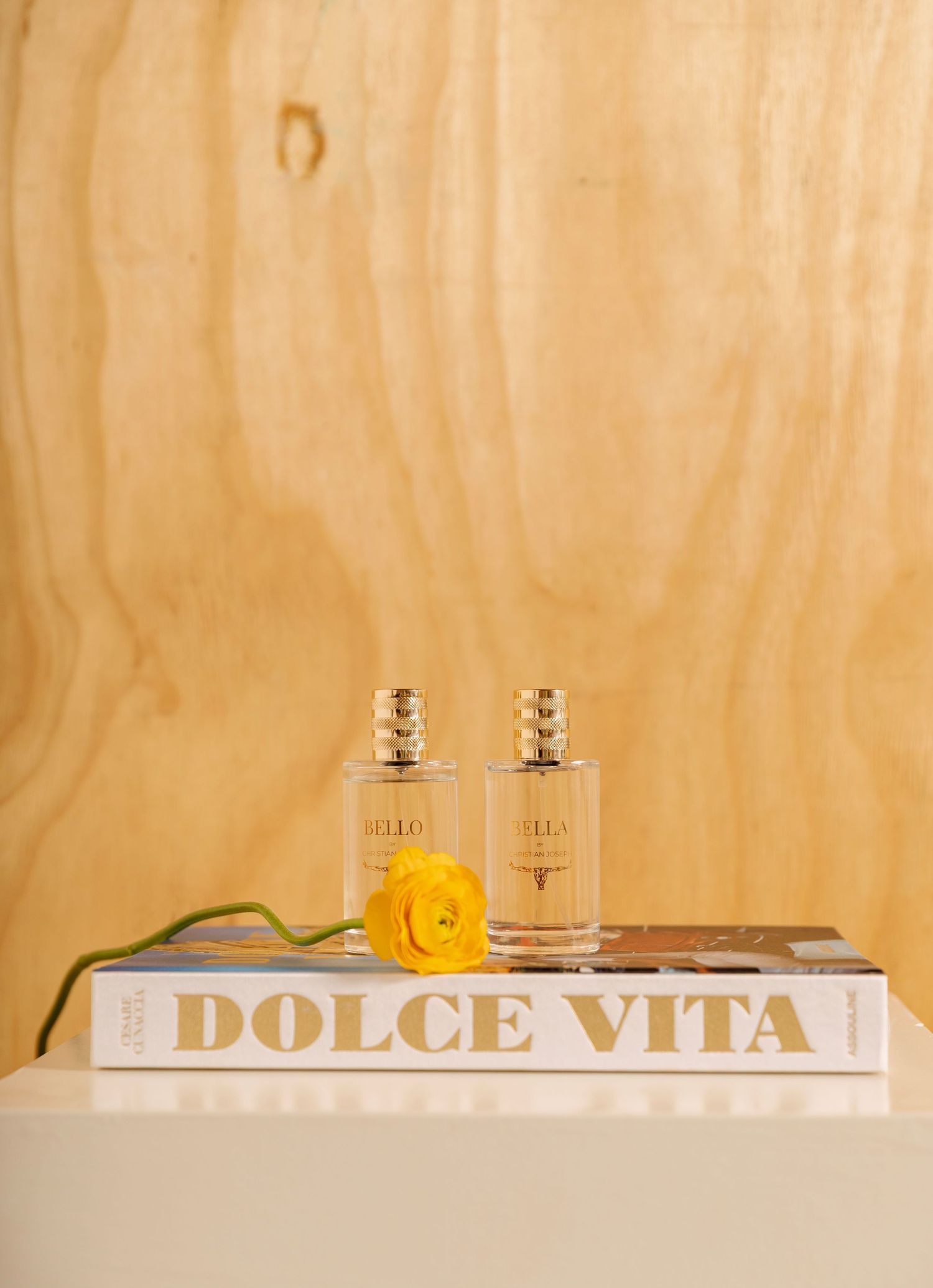 Minimalist composition of white and gold perfume bottles arranged on beige background with 'Dolce Vita' text.