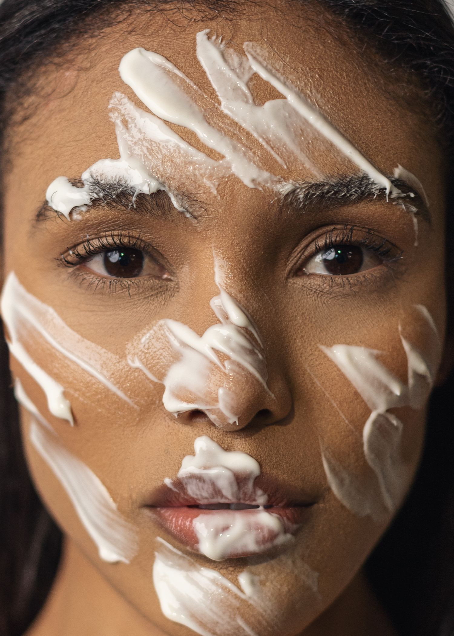 Creative beauty portrait showing white face paint applied in diagonal streaks across dark skin in an artistic pattern.