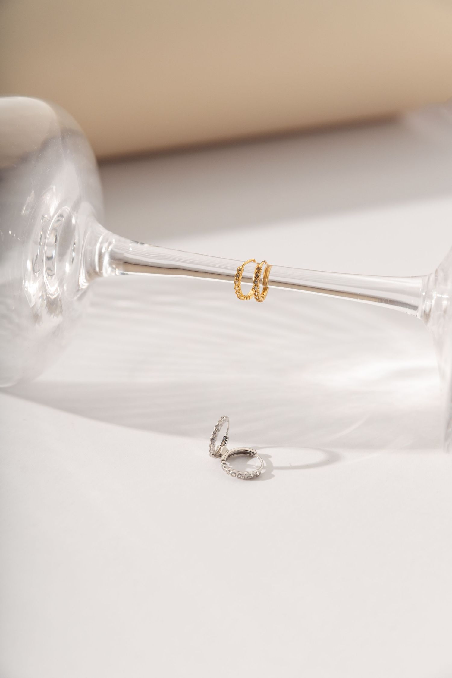 Small gold hoop earrings rest on a curved glass surface creating an artistic minimalist composition.