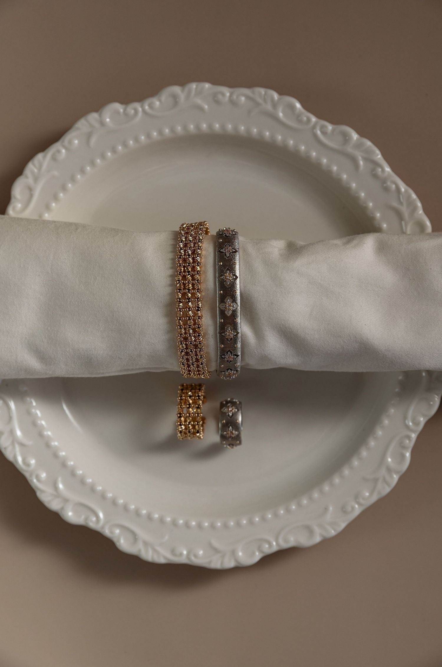 Elegant white ceramic plates with scalloped edges display gold and silver metallic napkin rings in a decorative table setting.