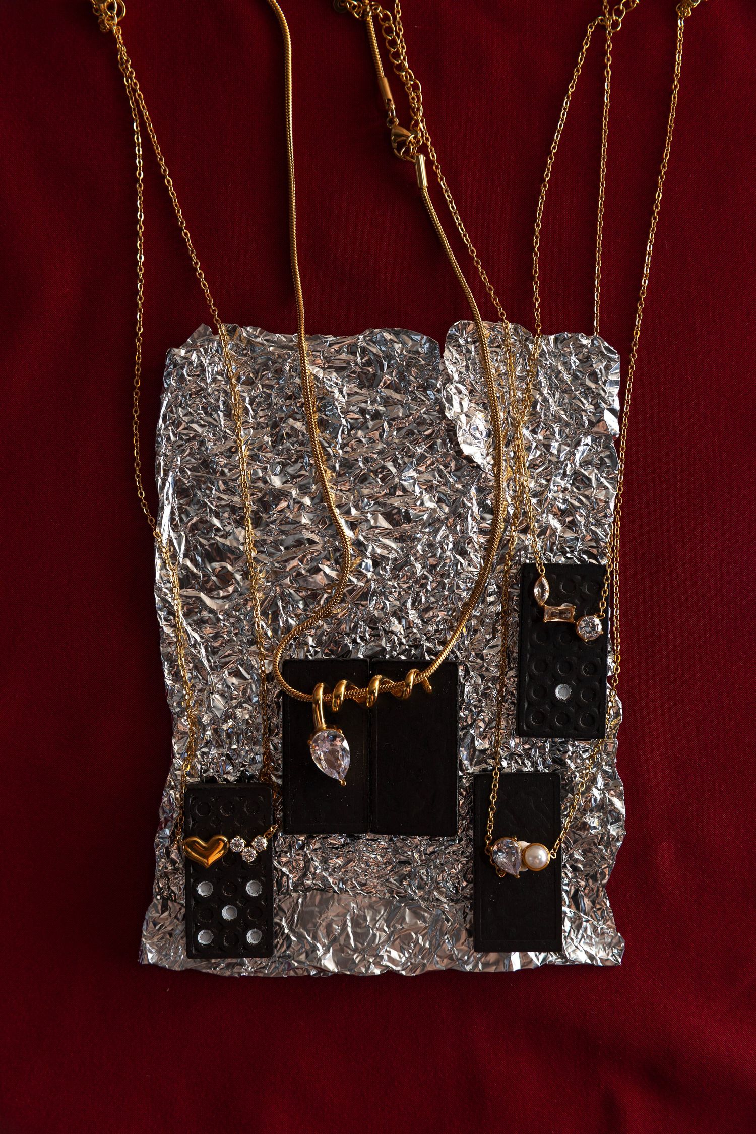 Three pieces of silver foil wrapped electronic components hang from brown strings against a dark red background.