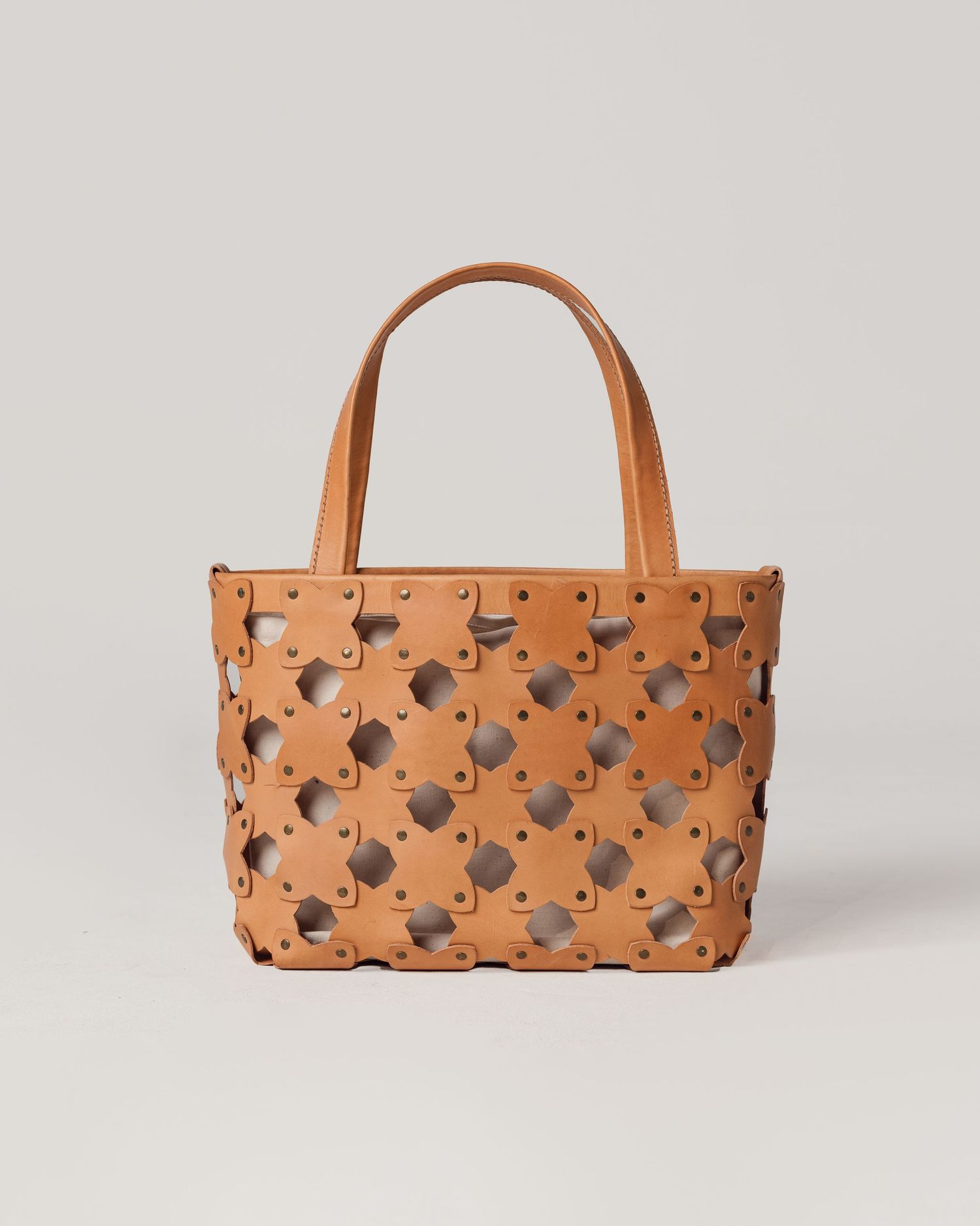 Stylish tan leather tote bag with geometric cutout pattern and double handles against light gray background.