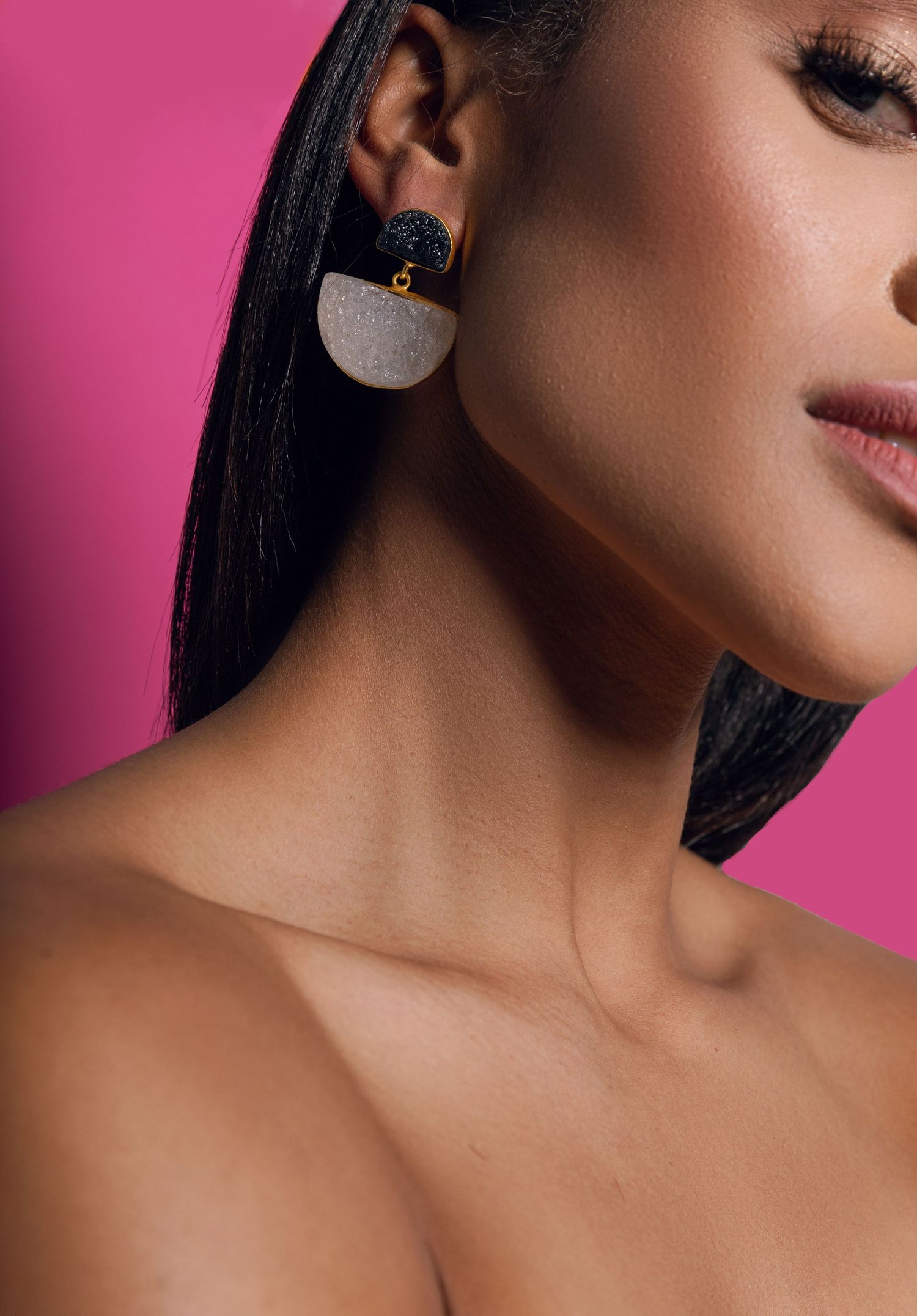 Close-up fashion portrait showing a modern geometric earring against a vibrant pink background.