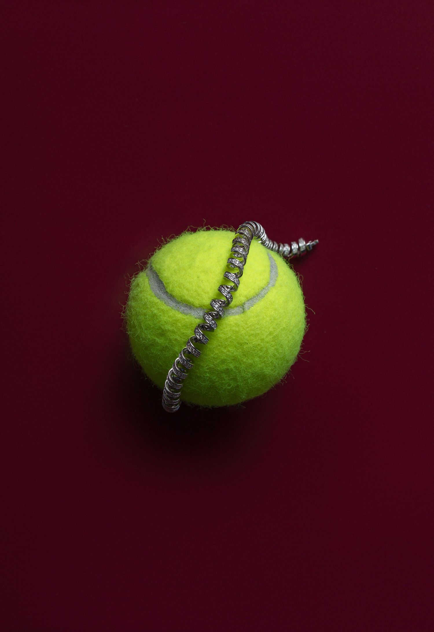 A bright yellow tennis ball pierced diagonally by a metal screw on a dark red background.