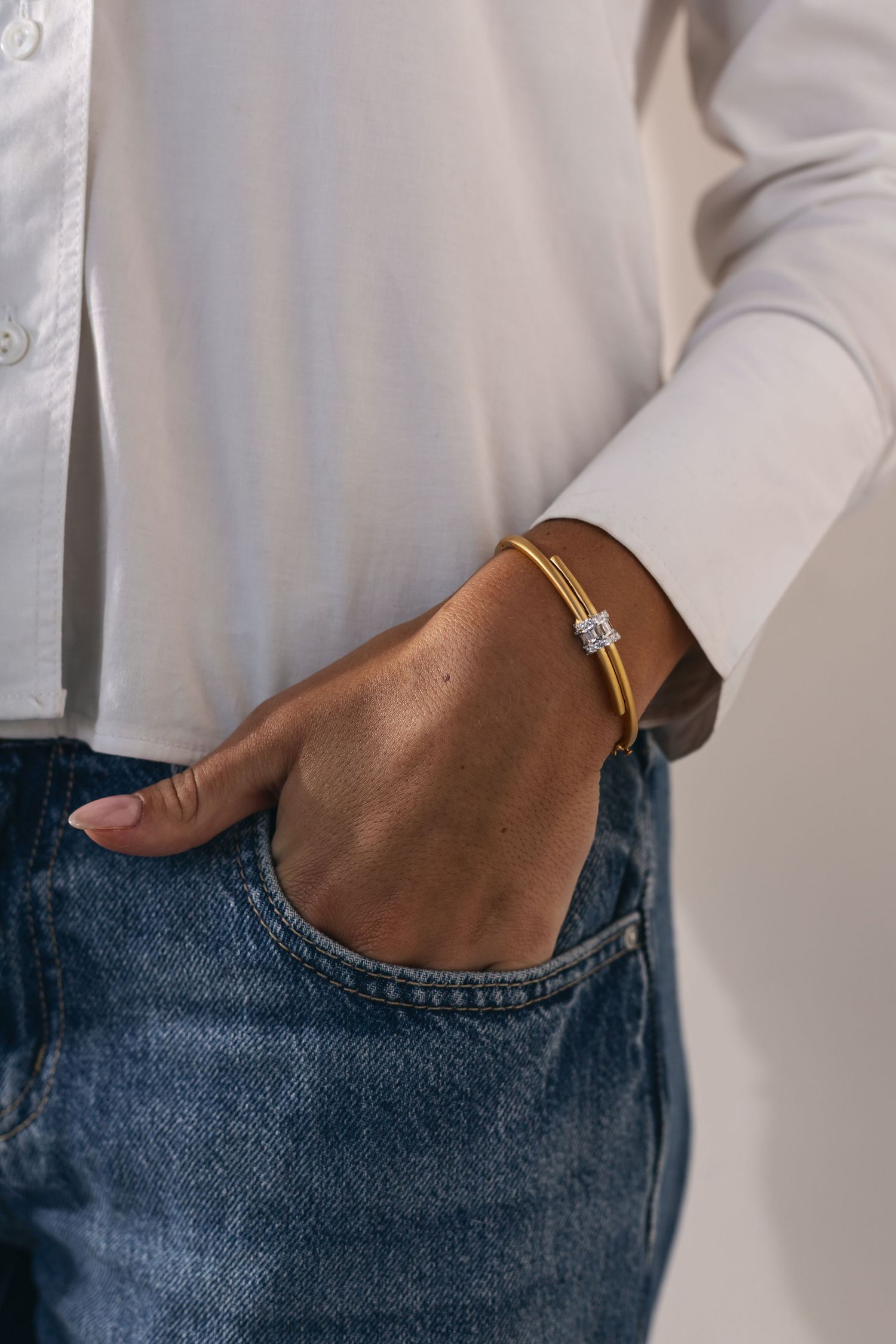 Gold and silver rings with gemstones adorned on feminine hands wearing crisp white blouse and vintage denim jeans.