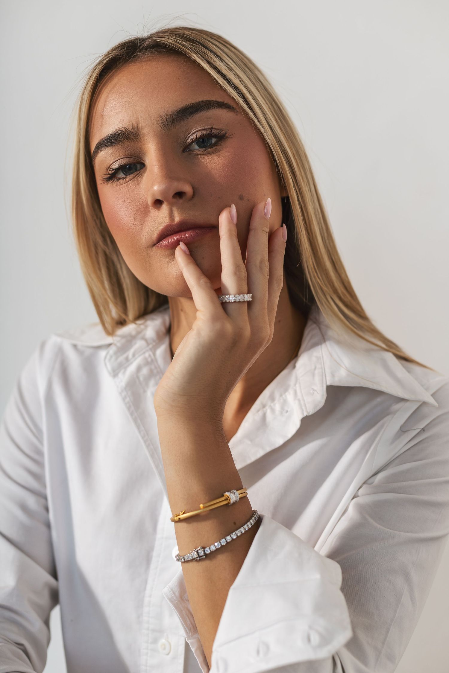 Fashion portrait featuring delicate jewelry including rings and bracelets worn with a crisp white button-down shirt.