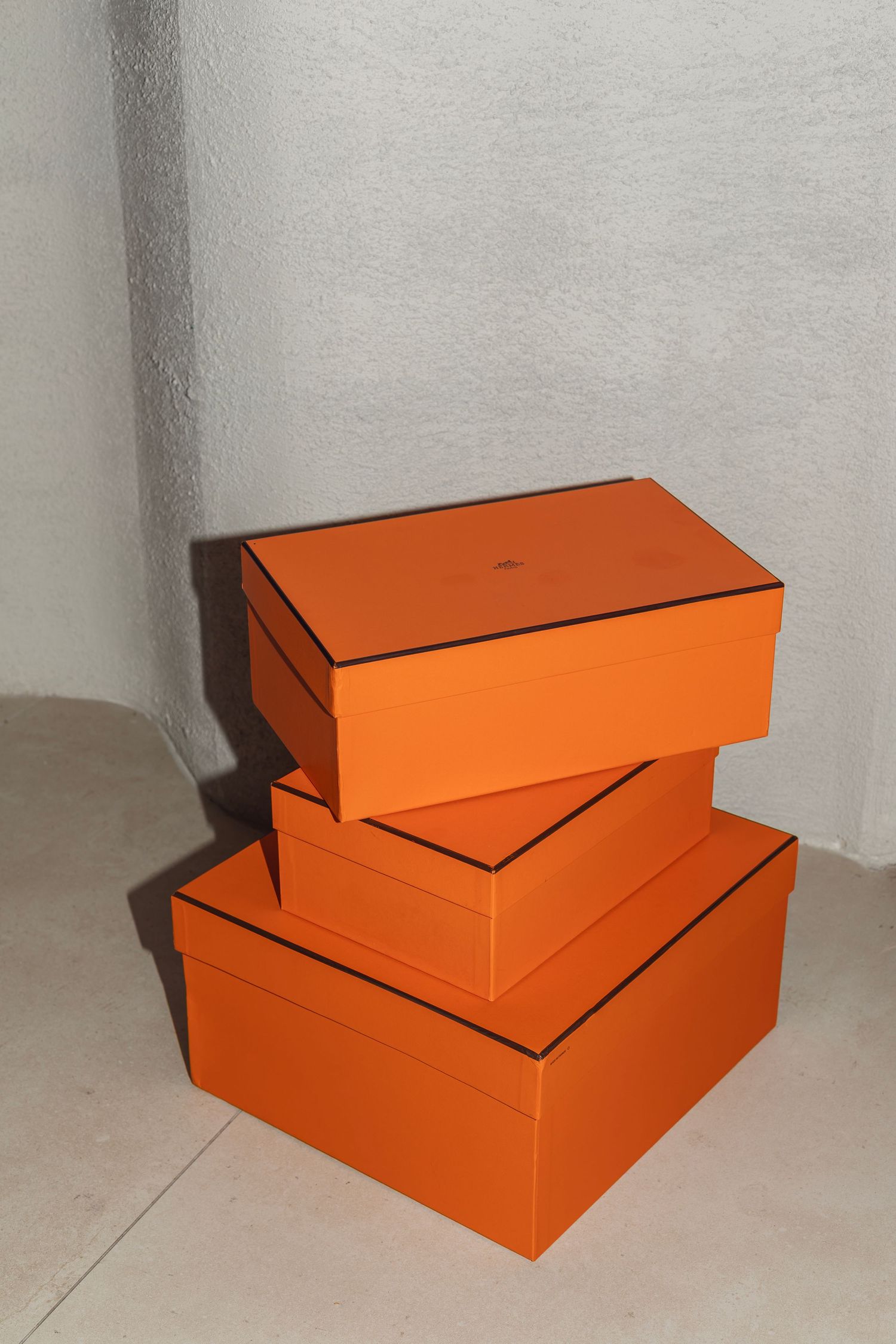 Three stacked orange storage boxes with black trim casting shadows against a white wall.