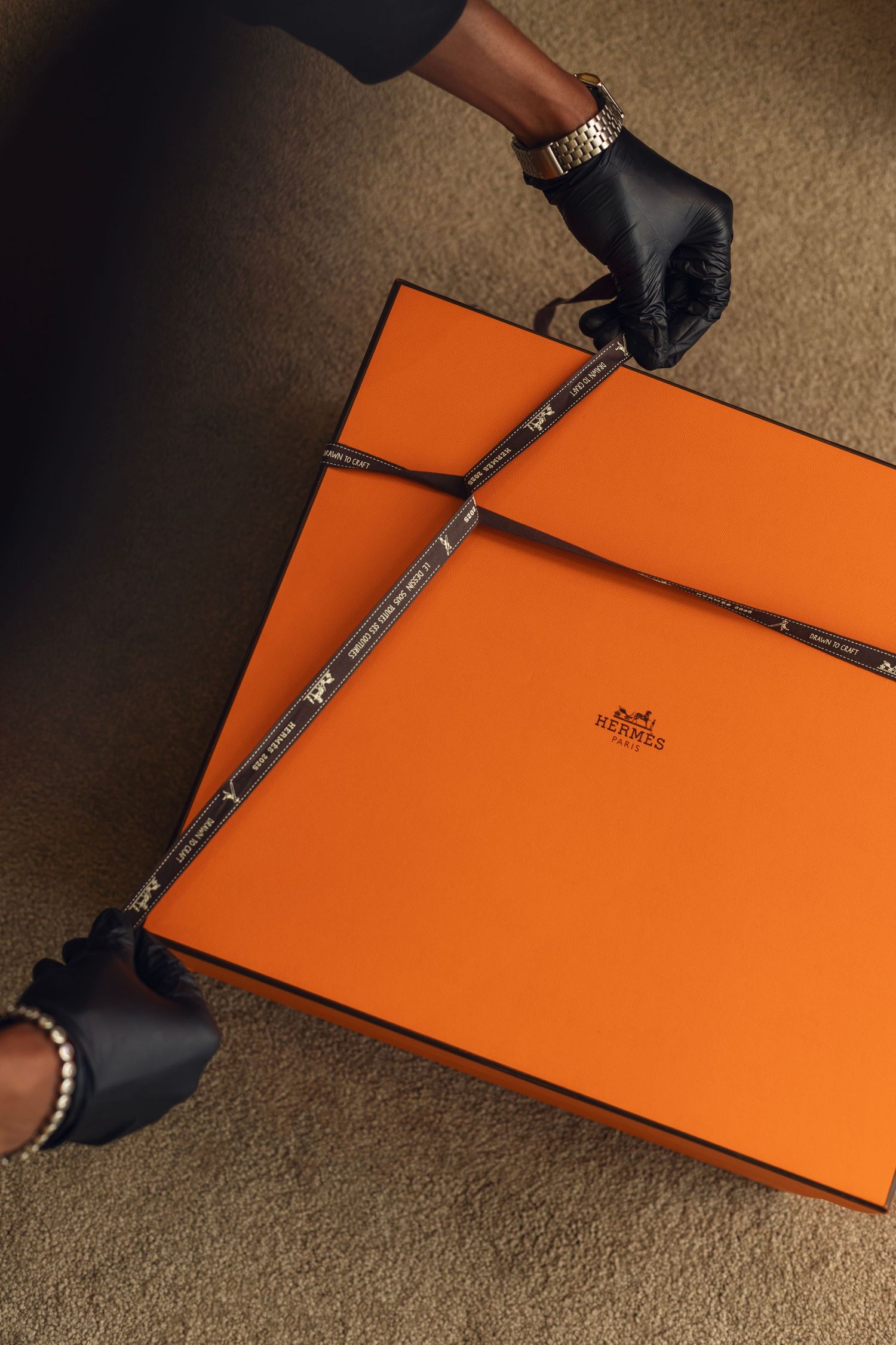 A step-by-step sequence showing the opening of a distinctive orange Hermes retail box with black ribbon detail.