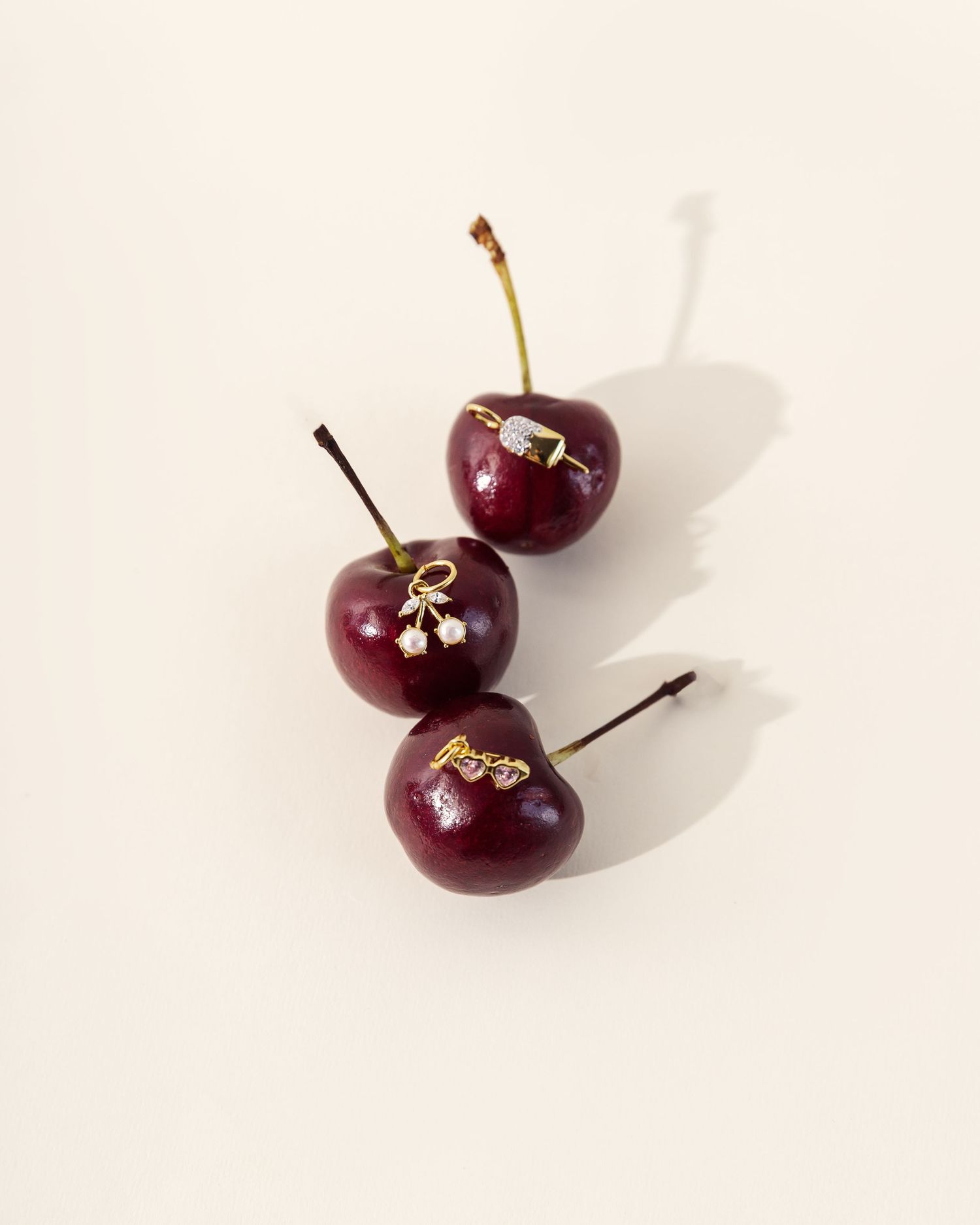 Three ripe dark red cherries arranged artistically on a plain light background with soft shadows.