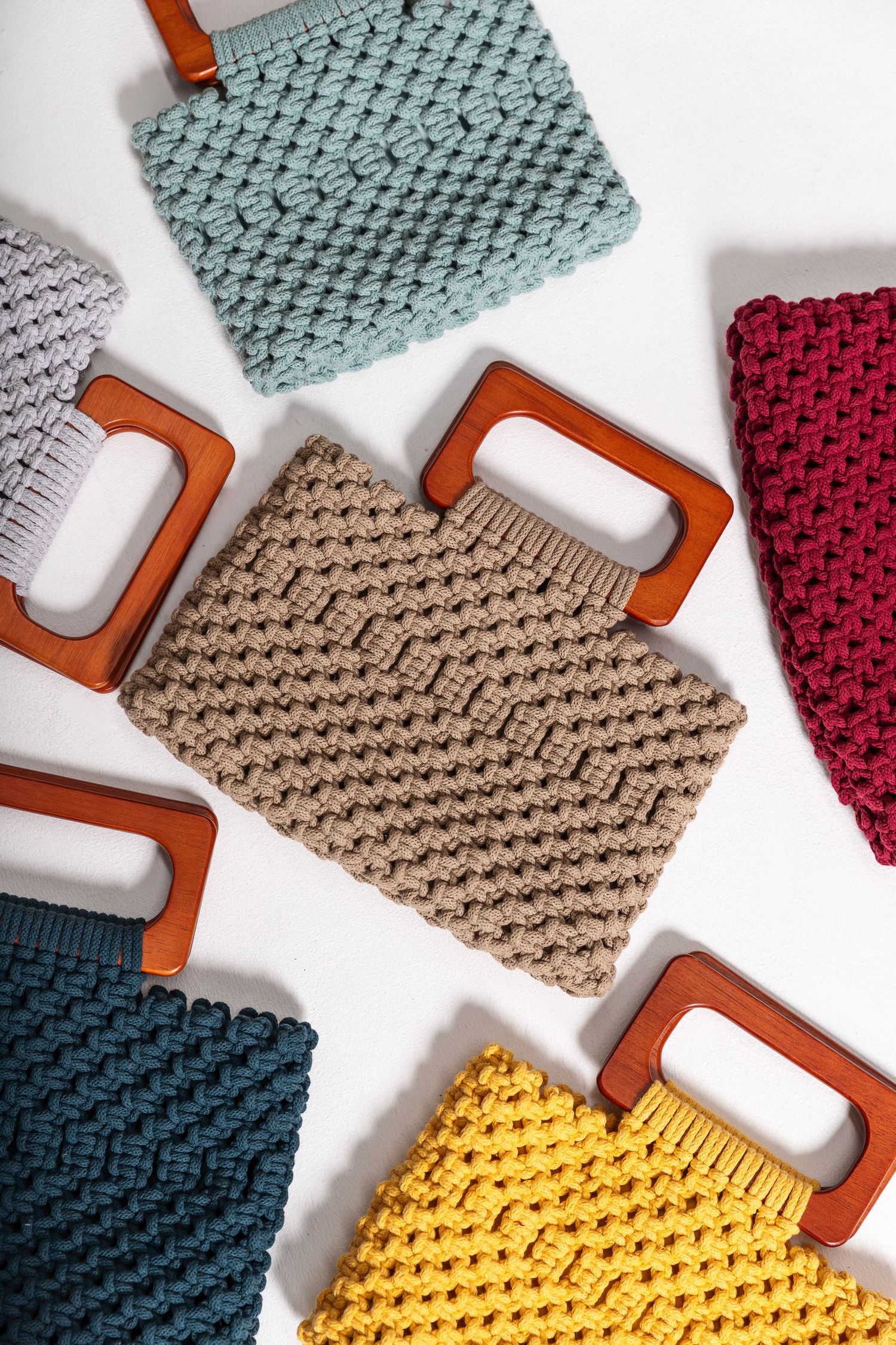 Colorful knitted handbags with wooden square handles in gray, blue, beige, red, teal, and yellow on white background.