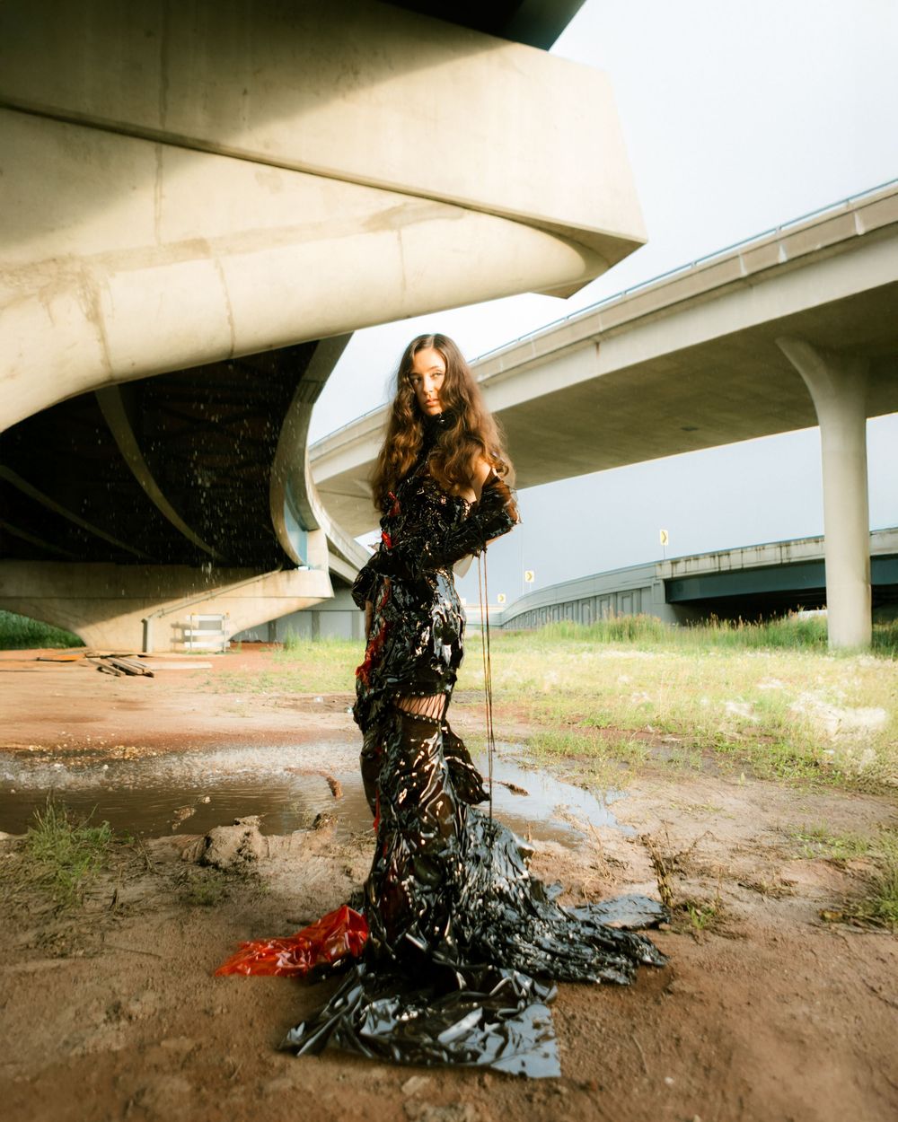 A figure in an elegant black lace gown poses underneath a concrete highway overpass in dramatic fashion photography.