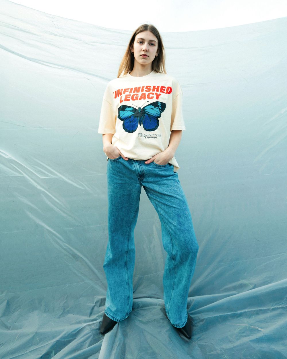 Casual outfit with white graphic t-shirt featuring blue butterfly print and wide-leg blue jeans against light blue backdrop.
