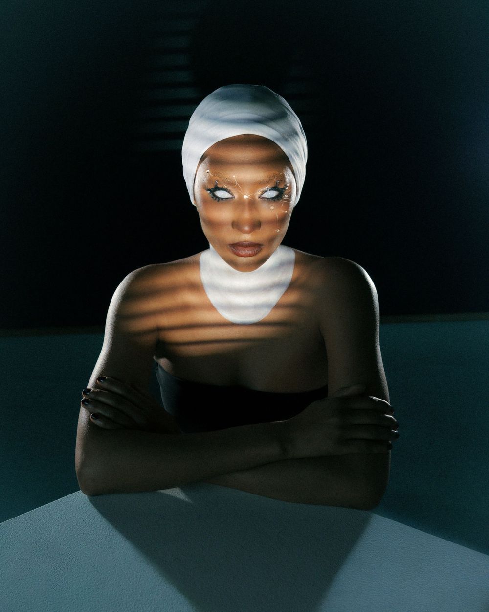 Artistic fashion portrait with dark background showing dramatic lighting and reflective surfaces.
