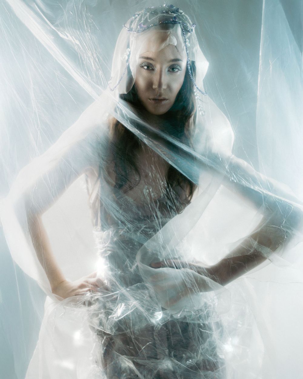 Ethereal artistic portrait wrapped in translucent plastic with moody lighting and fog effects creating a dreamy atmosphere.