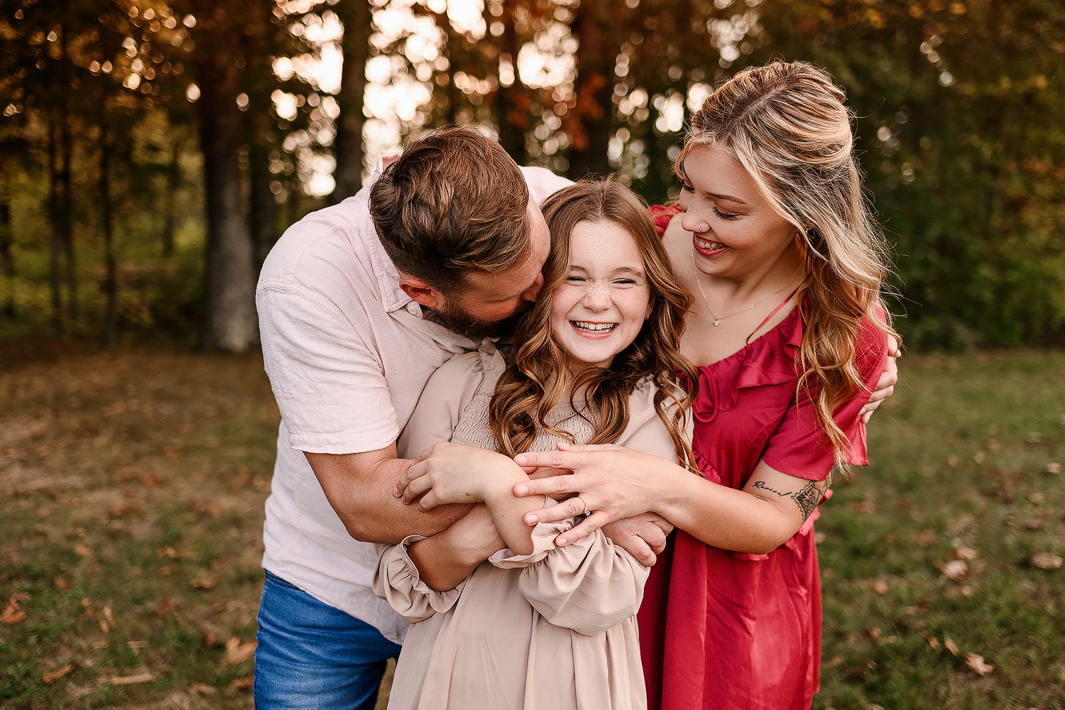 Happy family of three sharing a joyful moment outdoors in autumn, parents hugging their laughing young daughter.