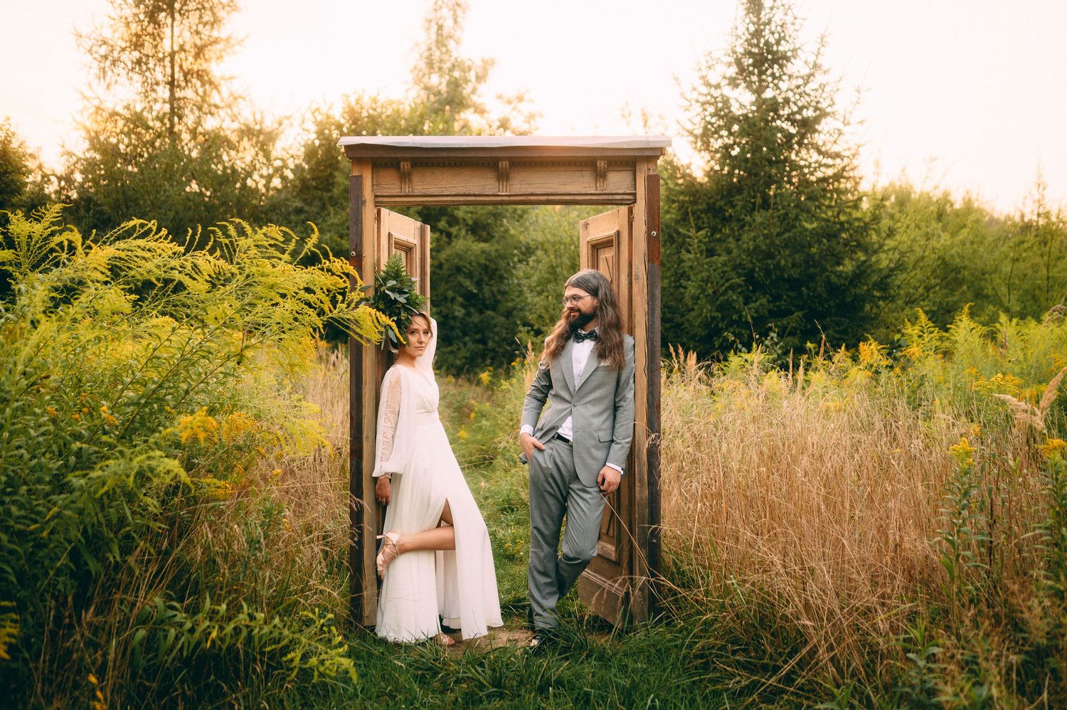 Rustic wooden archway framed by golden wildflowers and greenery at sunset.