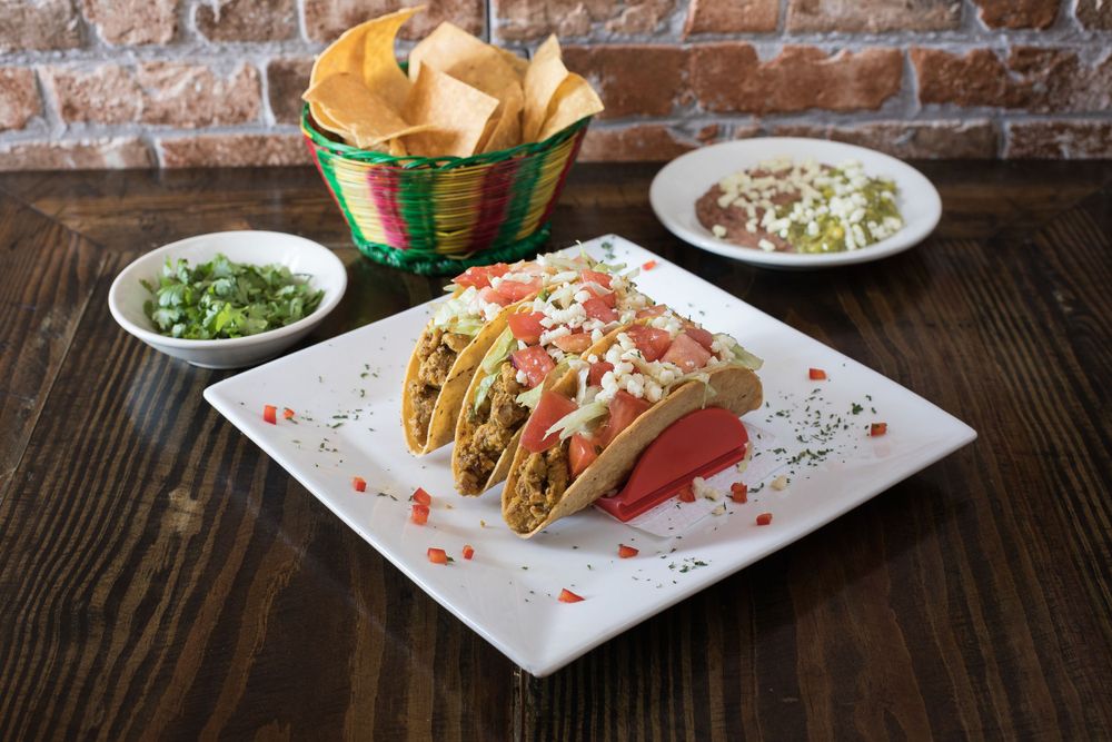 Mexican tacos served with salsa, guacamole and tortilla chips on wooden table.