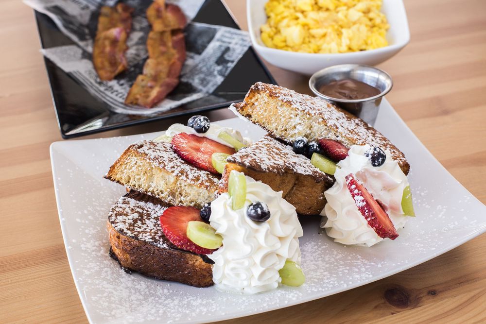 French toast with fresh fruit, whipped cream and powdered sugar served with bacon and eggs.