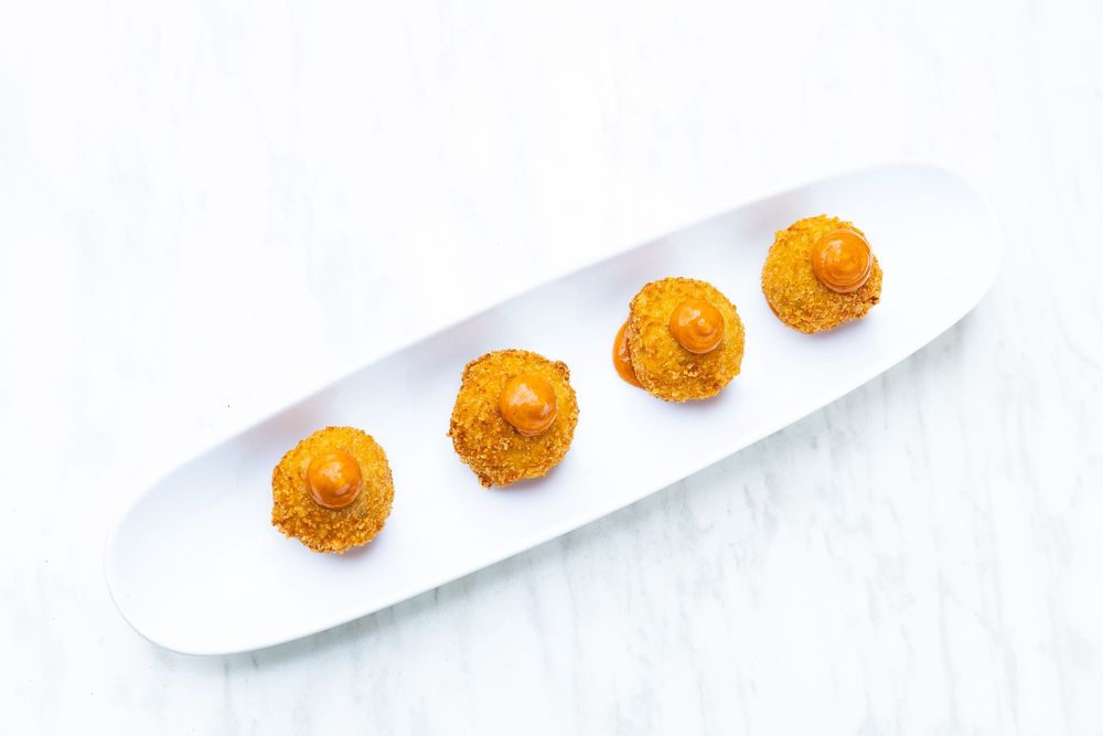 Four golden crispy croquettes arranged artfully on white rectangular plate.