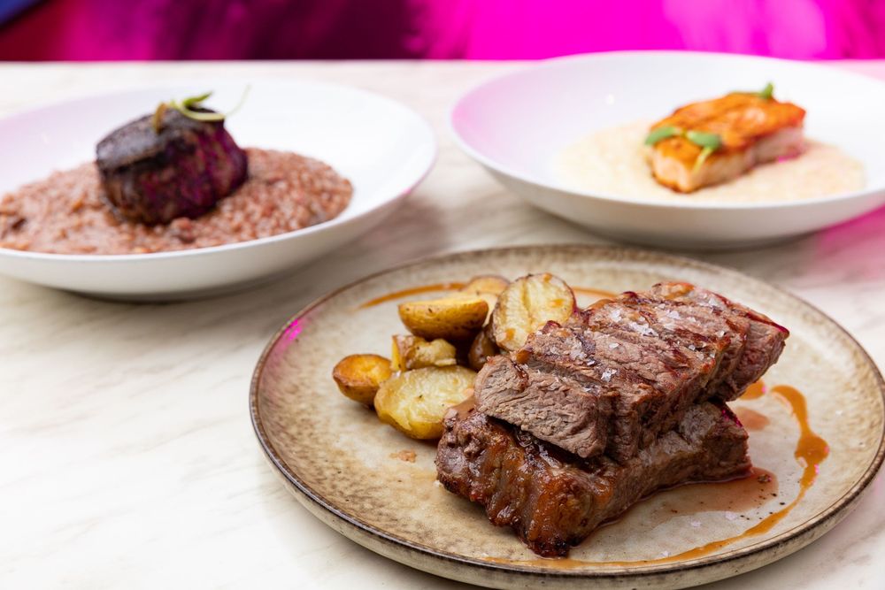 Gourmet beef ribs with roasted potatoes and sauce plated elegantly on ceramic dishes.