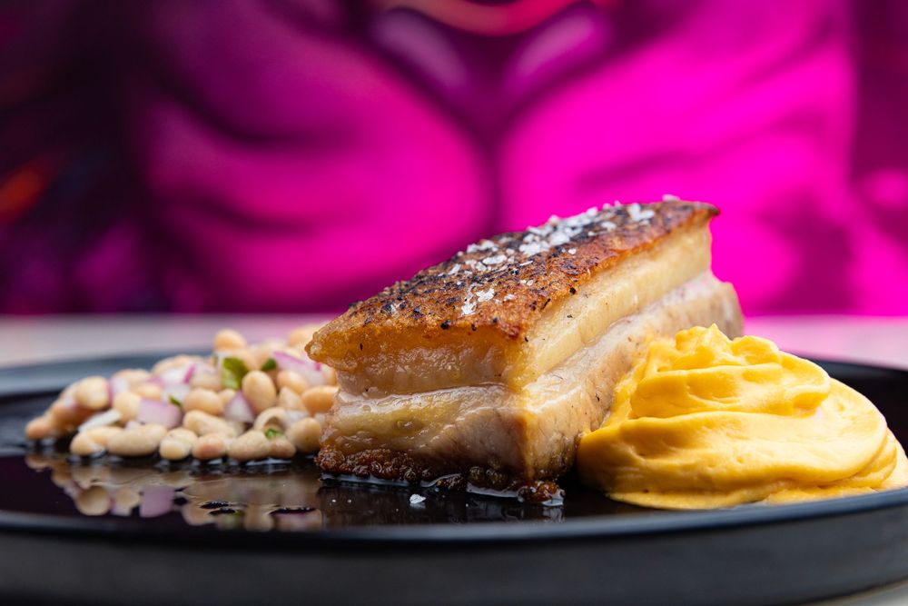 Crispy pork belly with mashed potatoes served on black plate with elegant presentation.