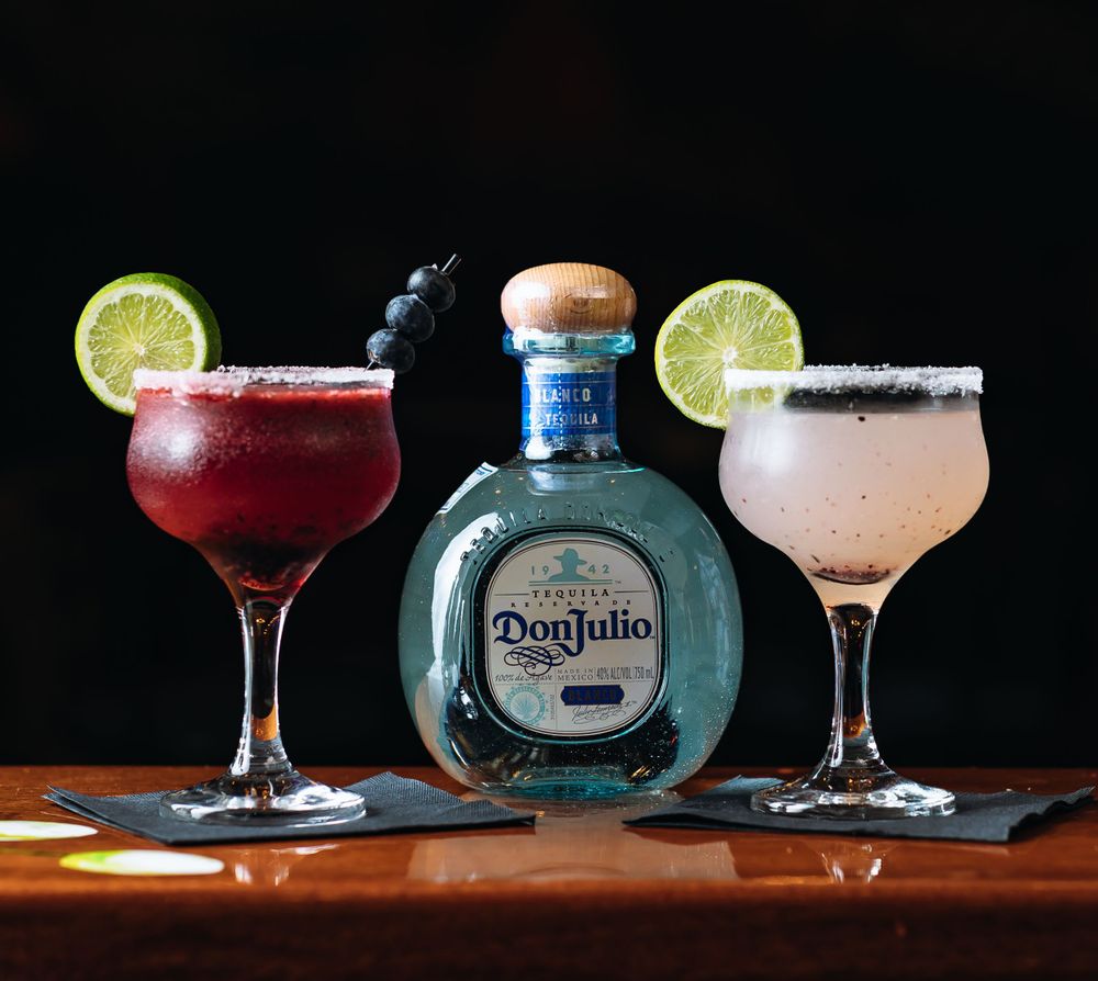 Don Julio tequila bottle with two margarita cocktails garnished with lime slices.